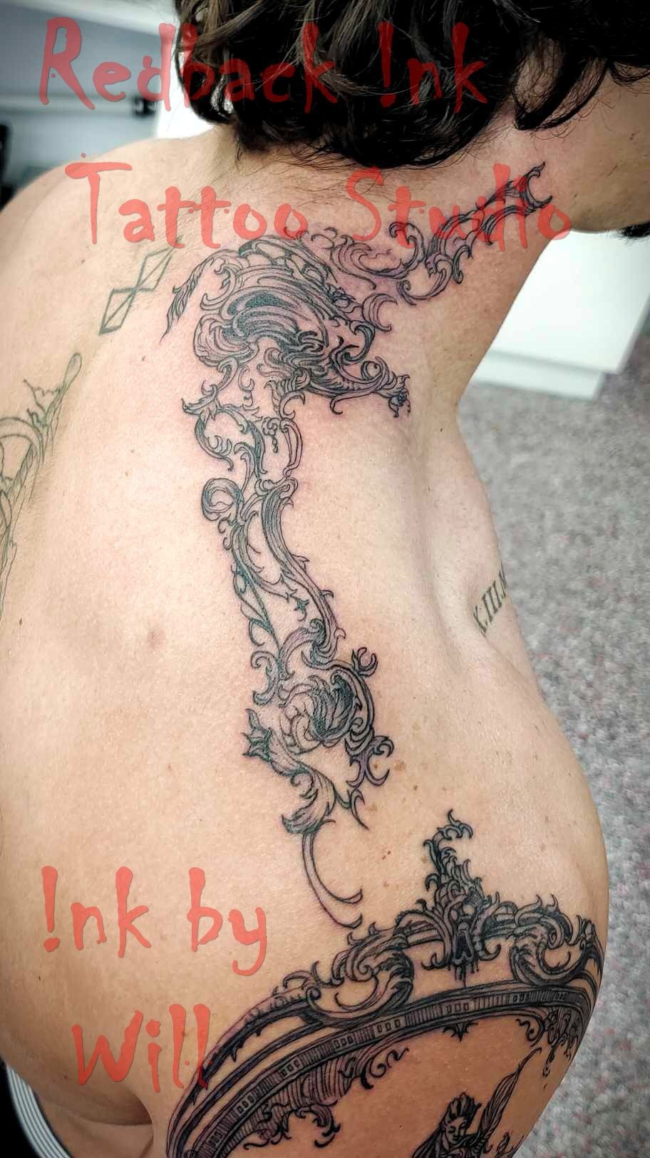 Tattoo of ornate design on person's back and neck. Black ink, studio setting.