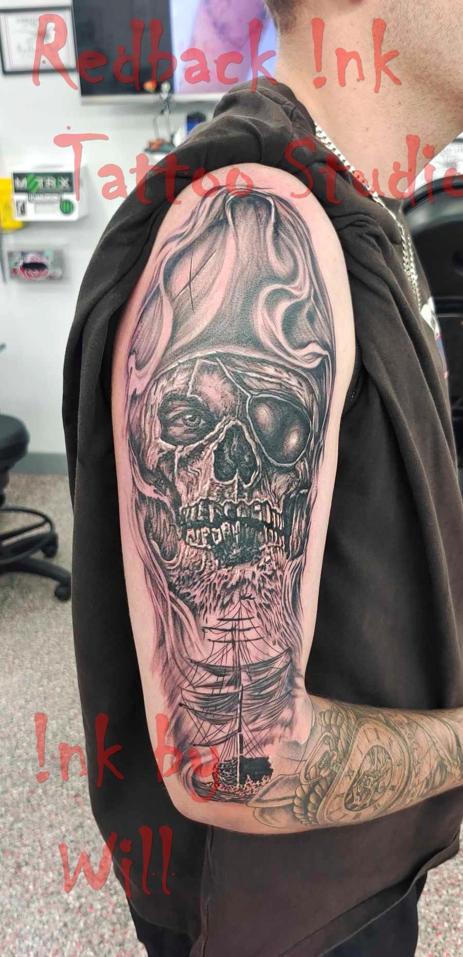 Pirate skull tattoo on a man's arm; black and grey shading. Red Ink Tattoo Studio logo in upper left corner.
