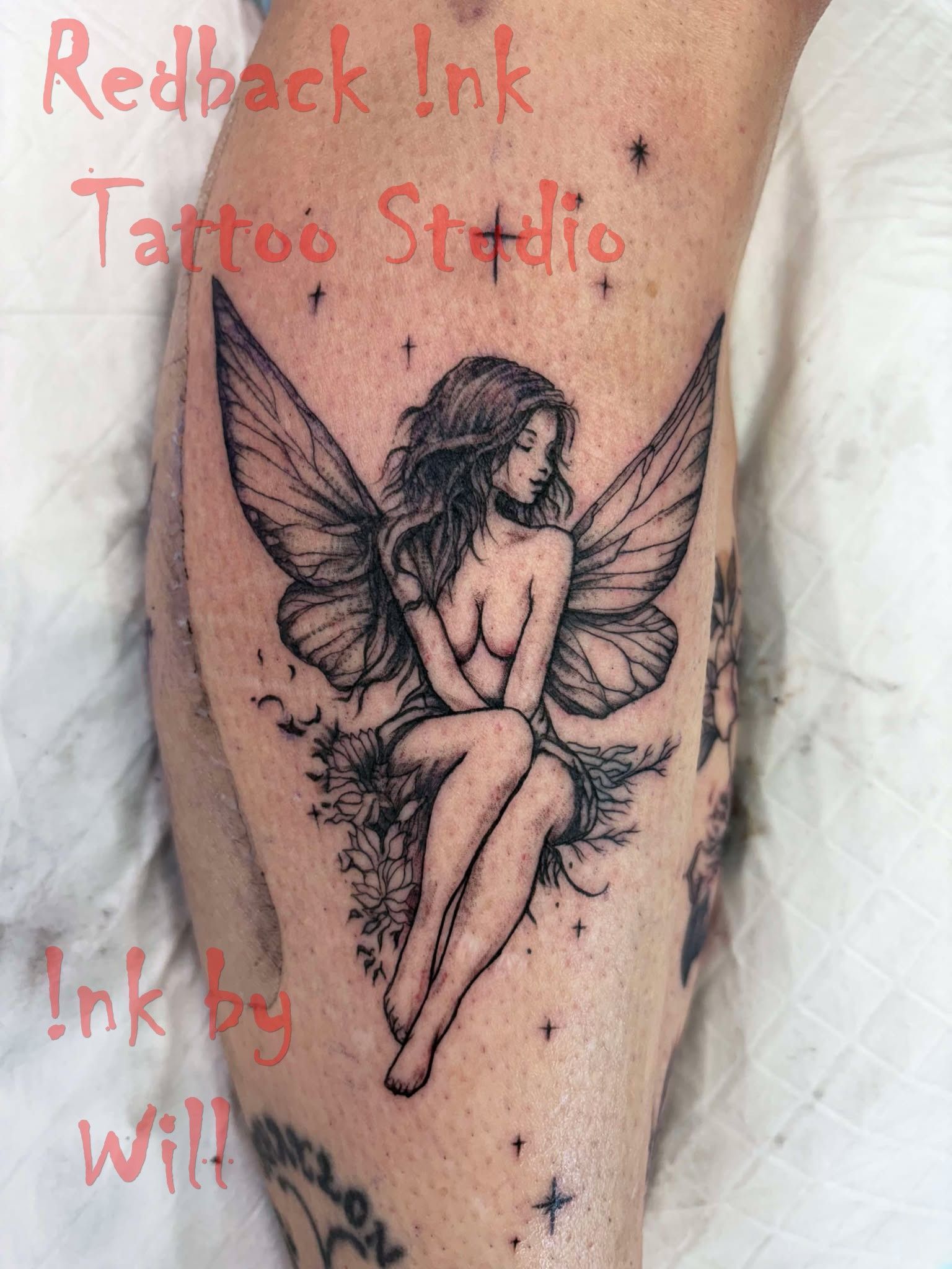 Tattoo of a fairy sitting on a bed of flowers with wings. Black ink on the leg.