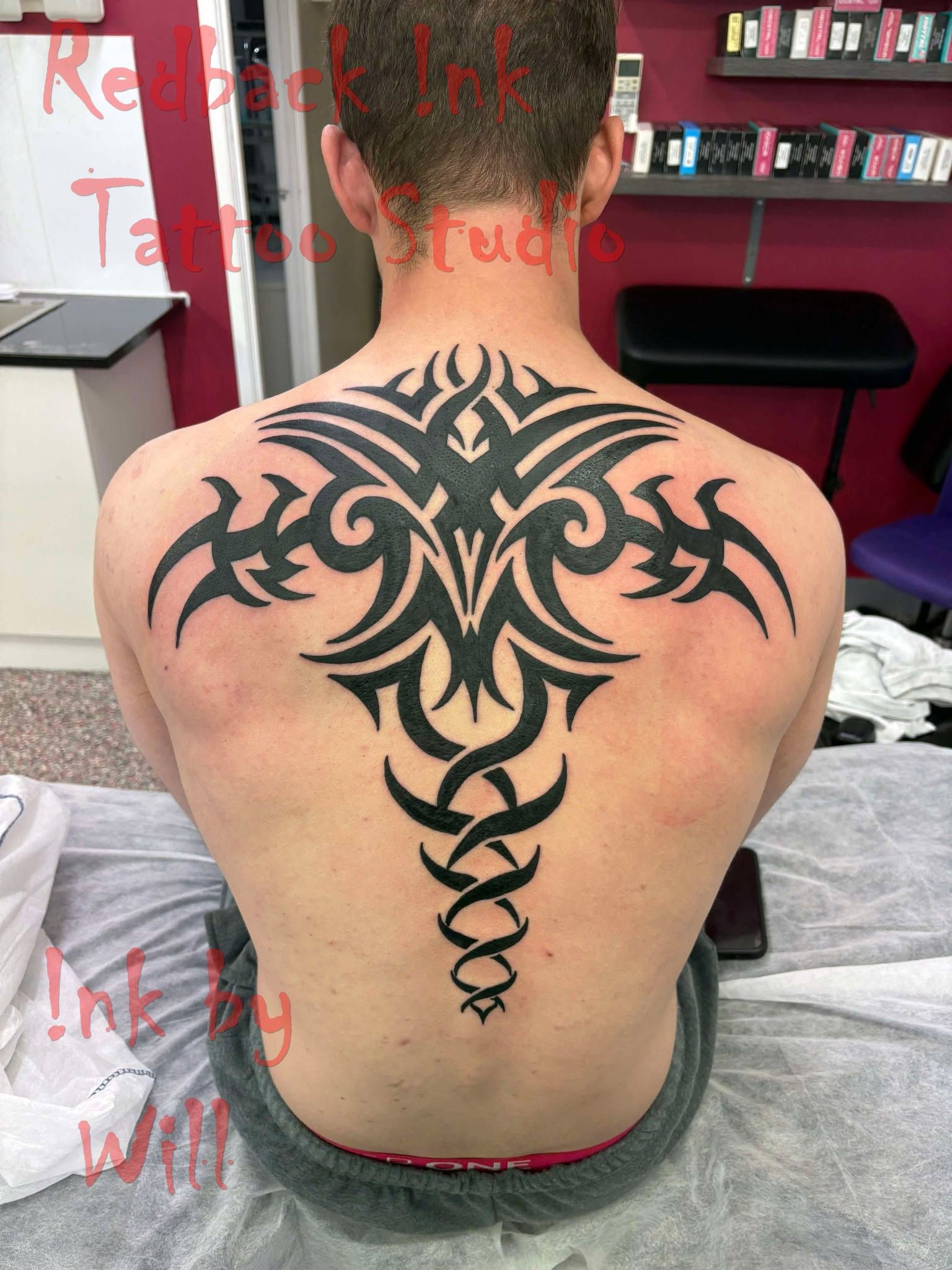 Man's back with large black tribal tattoo in a studio setting.