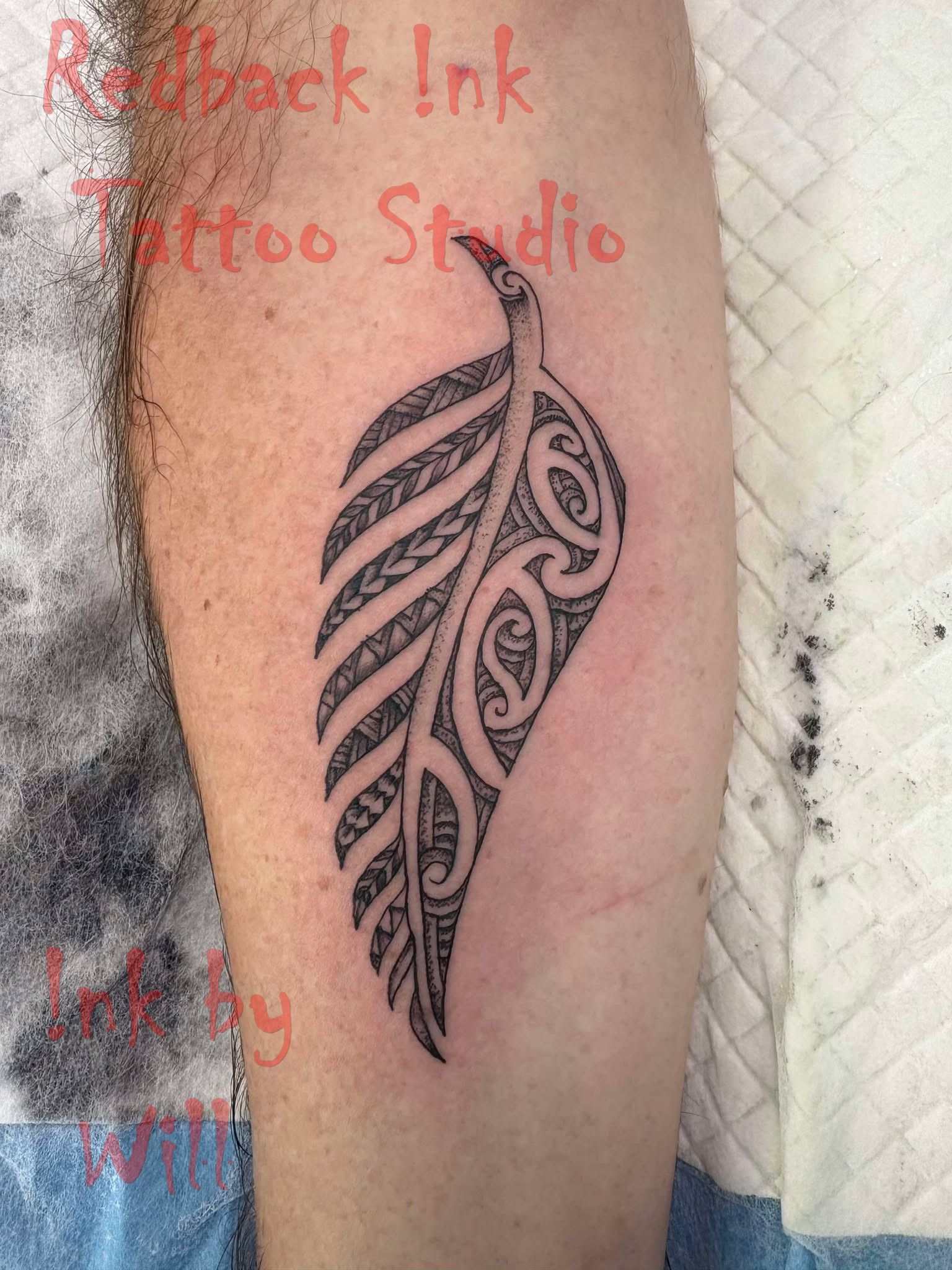 Black tribal leaf tattoo on a person's leg, in a studio setting.