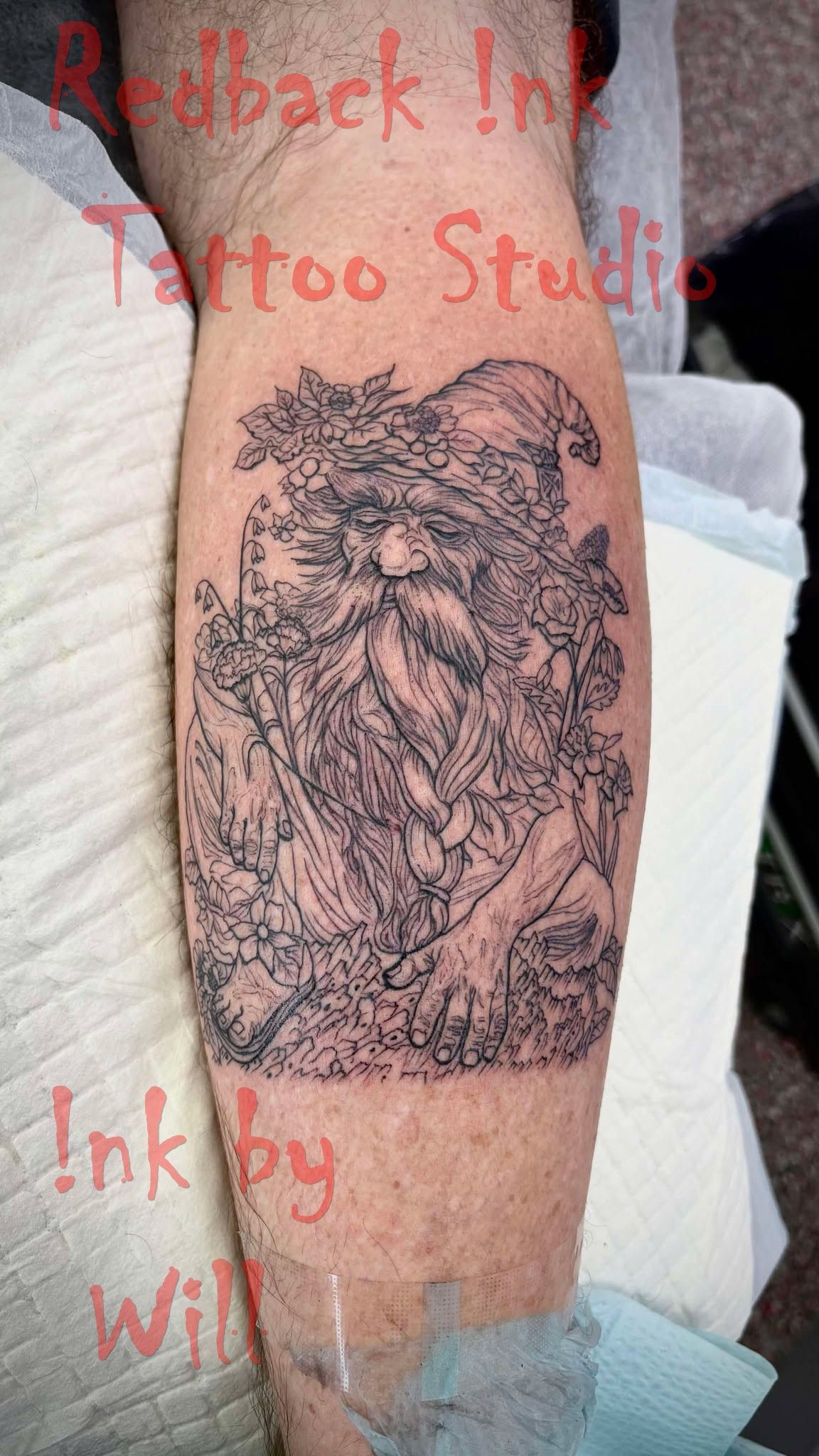 Tattoo of a bearded figure in a hat, on a leg, with Redback Ink Tattoo Studio text.