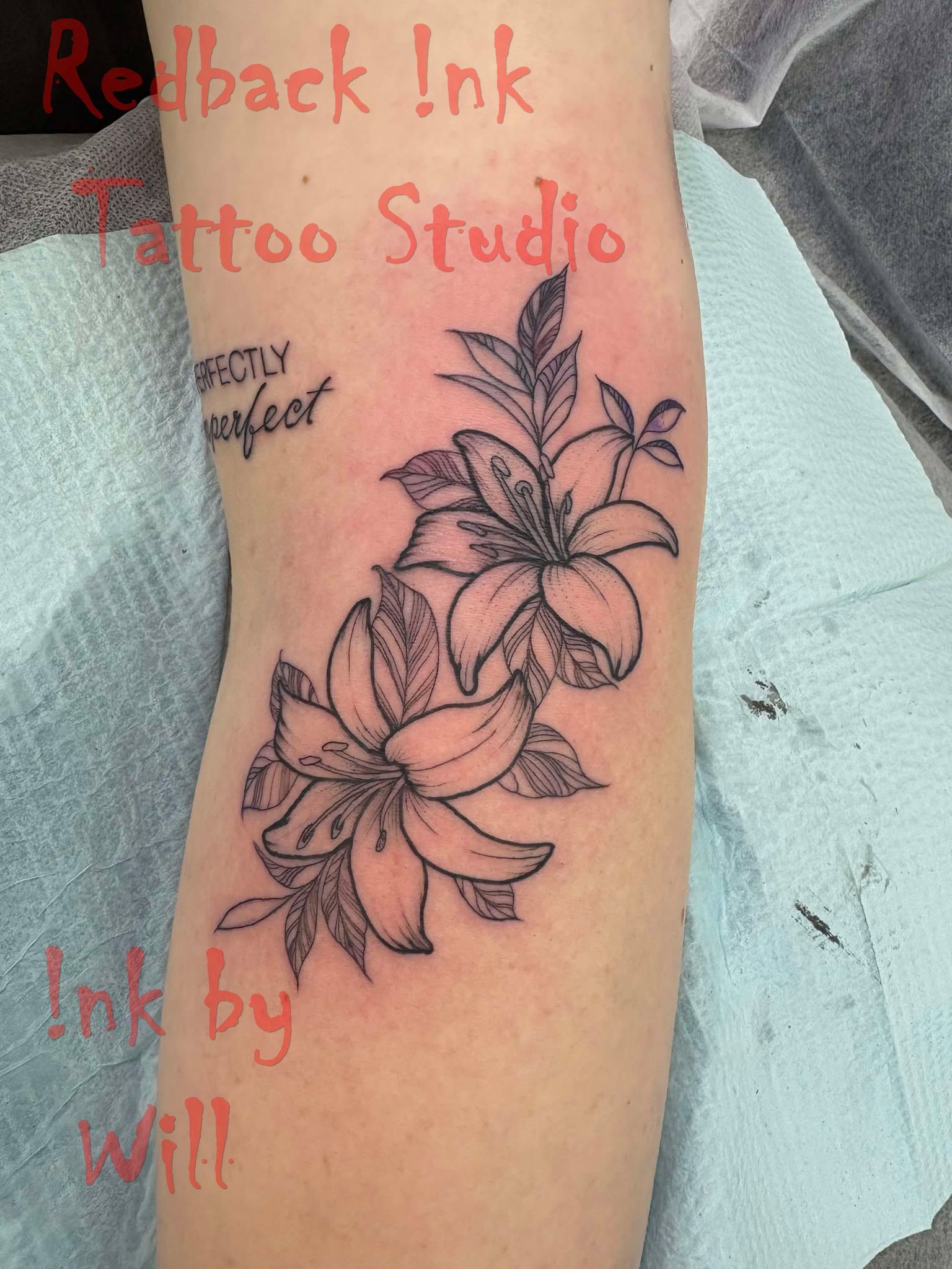 Tattoo of two lilies on an arm, outlined in black, with leaves. Red text: 