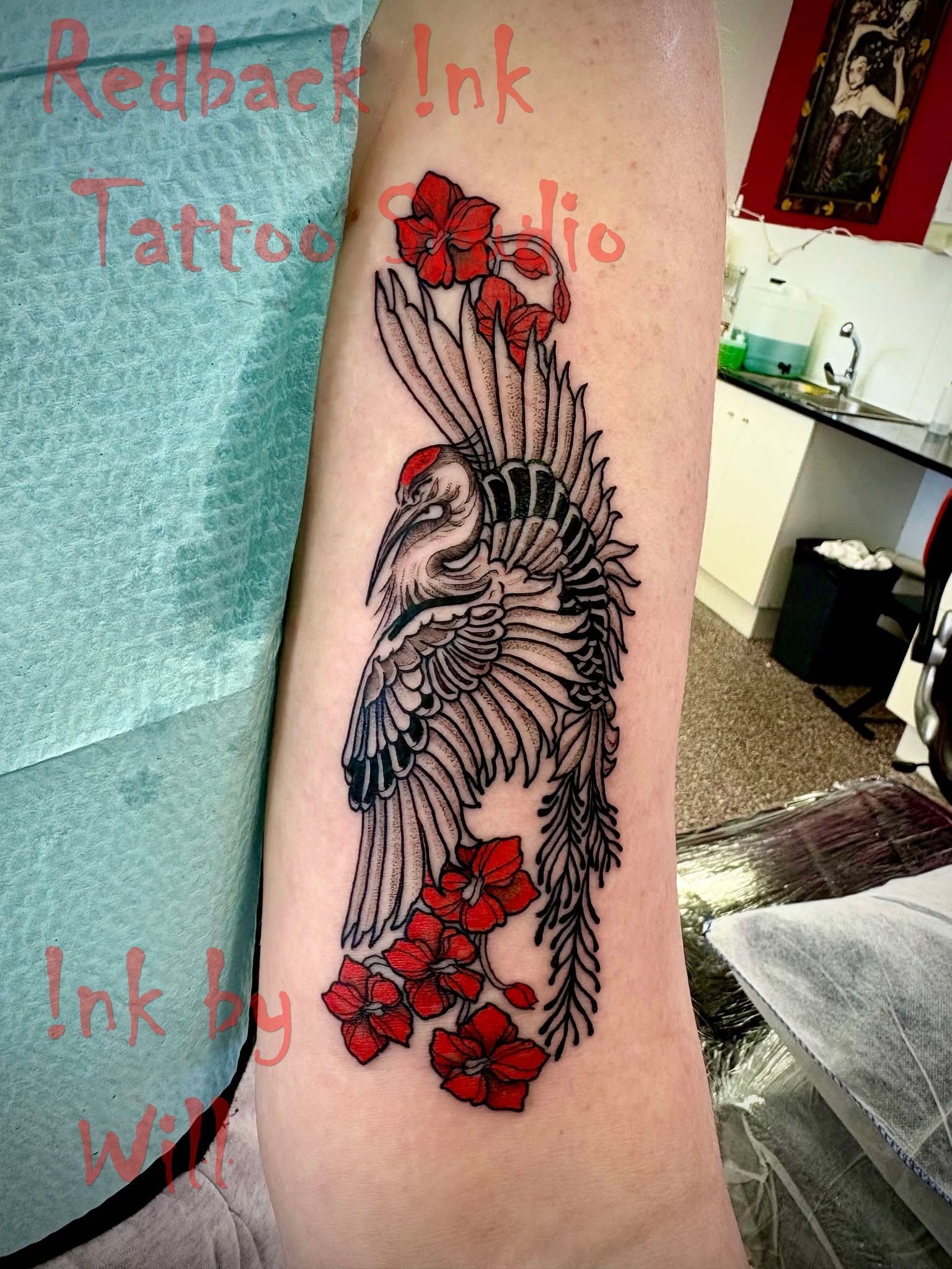 Tattoo of a crane with red flowers on an arm. Black and red ink. Studio setting.
