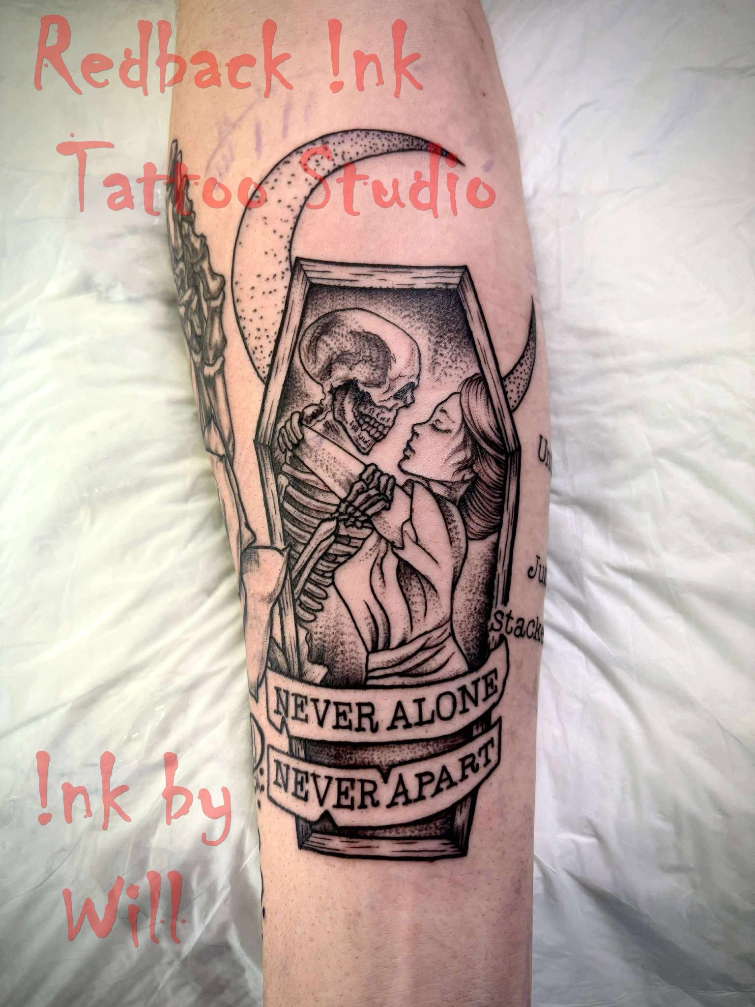 Tattoo of a skeleton and a woman embracing in a coffin under a crescent moon; text reads 