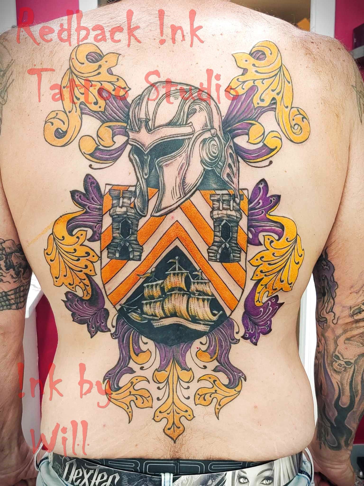 Man's back tattoo of a colorful coat of arms with a helmet, ship, and decorative flourishes.