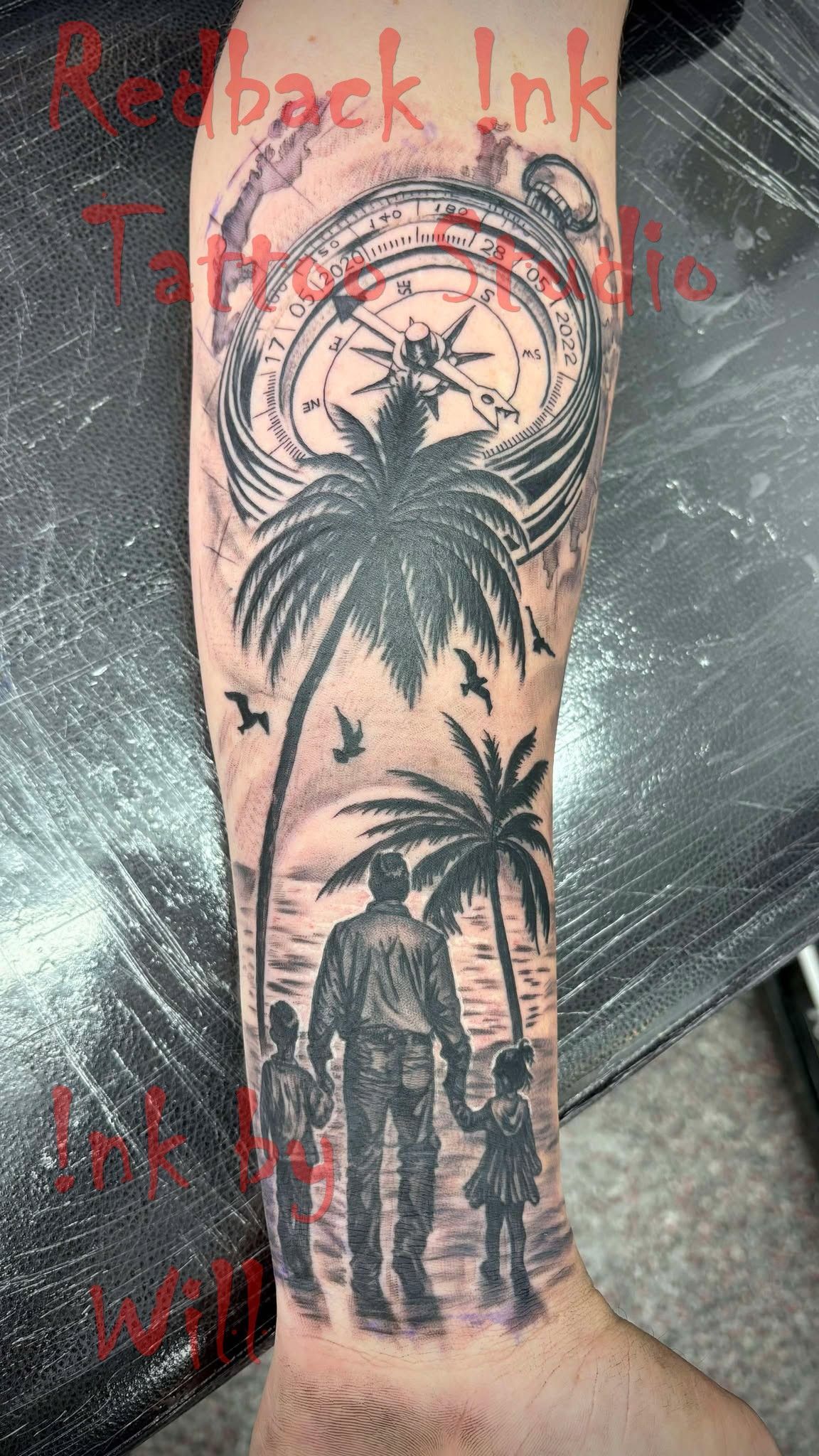 Tattoo of a father and two children walking on a beach, with palm trees and a compass design above.
