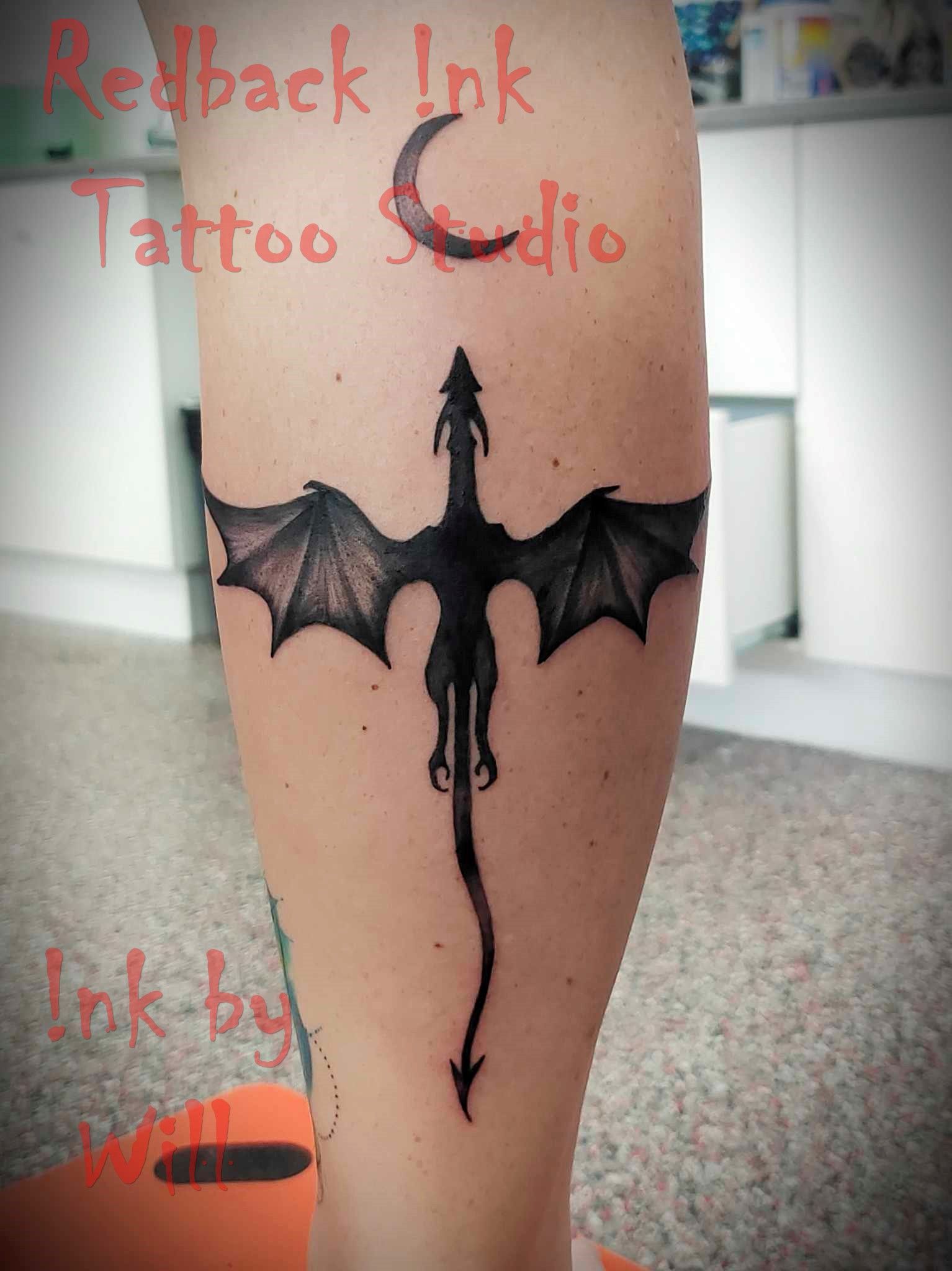 Dragon tattoo on an arm, black ink. A dragon with outstretched wings, crescent moon above — Redback !nk Tattoo Studio in Kawana, QLD