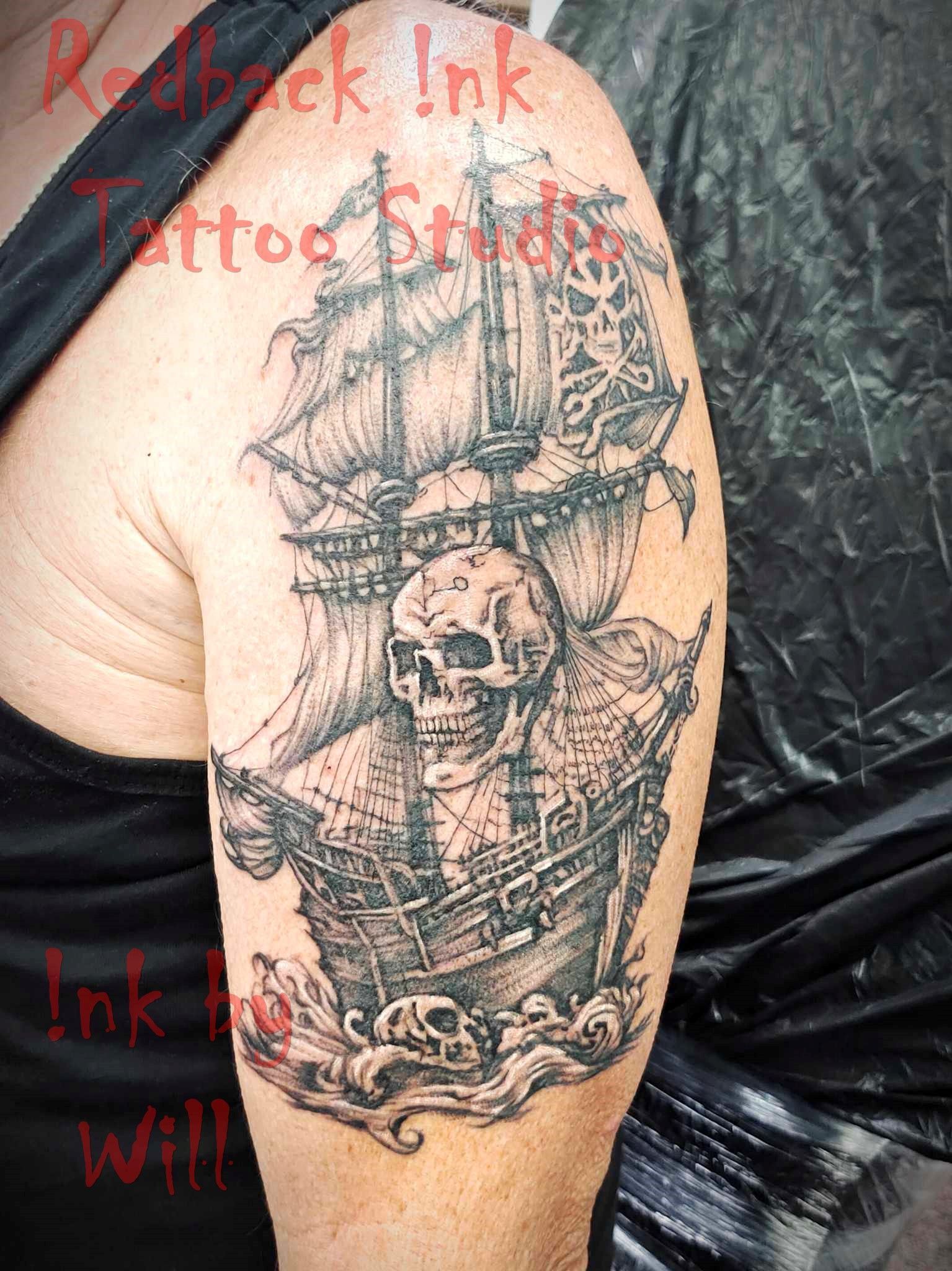 Pirate ship tattoo on upper arm featuring skull, waves, and ship details in black ink.