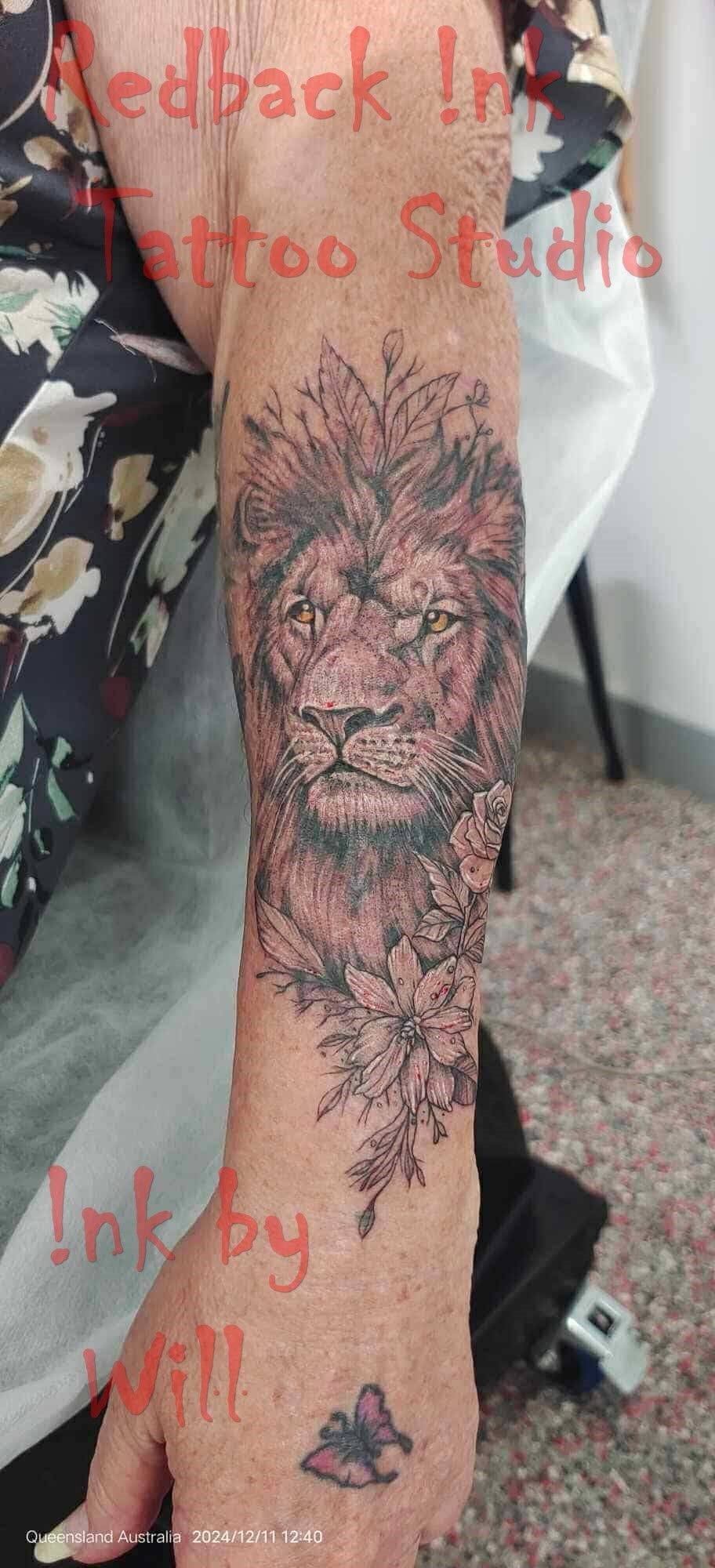 Lion tattoo on a person's arm, with a butterfly tattoo on their hand, and text overlay — Redback !nk Tattoo Studio in Kawana, QLD