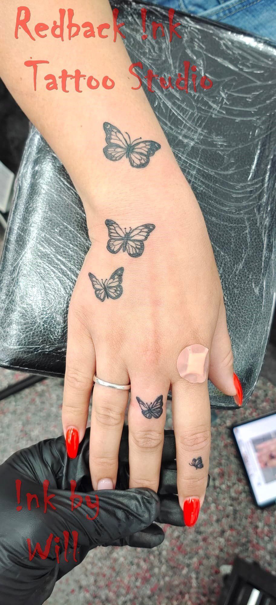 Hand with butterfly tattoos; a finger has a bandage and red nails.