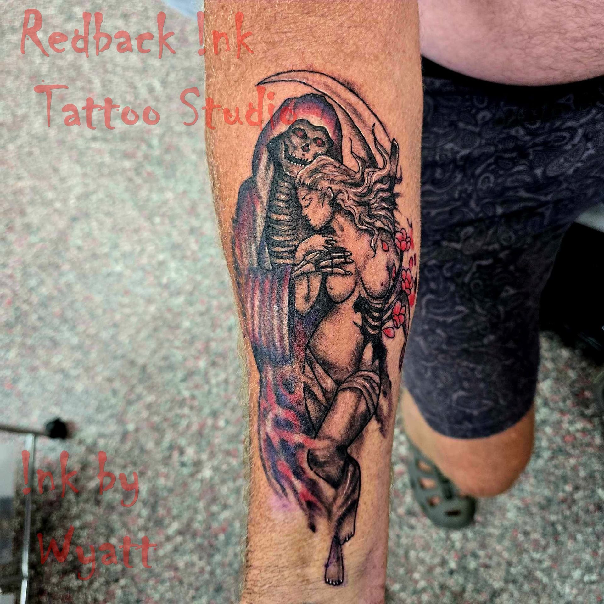 Tattoo on arm: Grim Reaper with scythe embracing a woman with cherry blossoms, done in shades of gray and red.