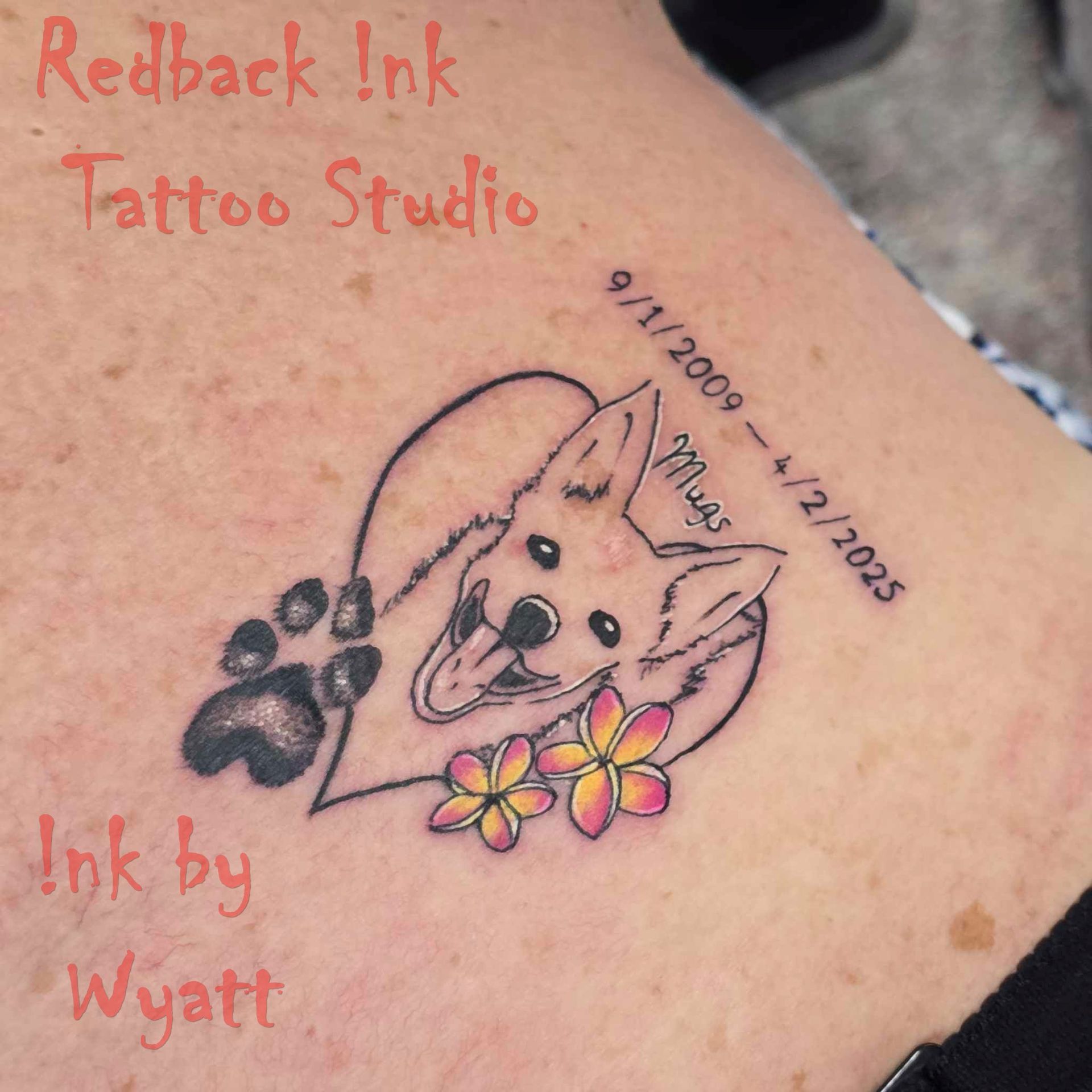 Tattoo of a dog inside a heart, paw print, flowers, dates, and artist's name.