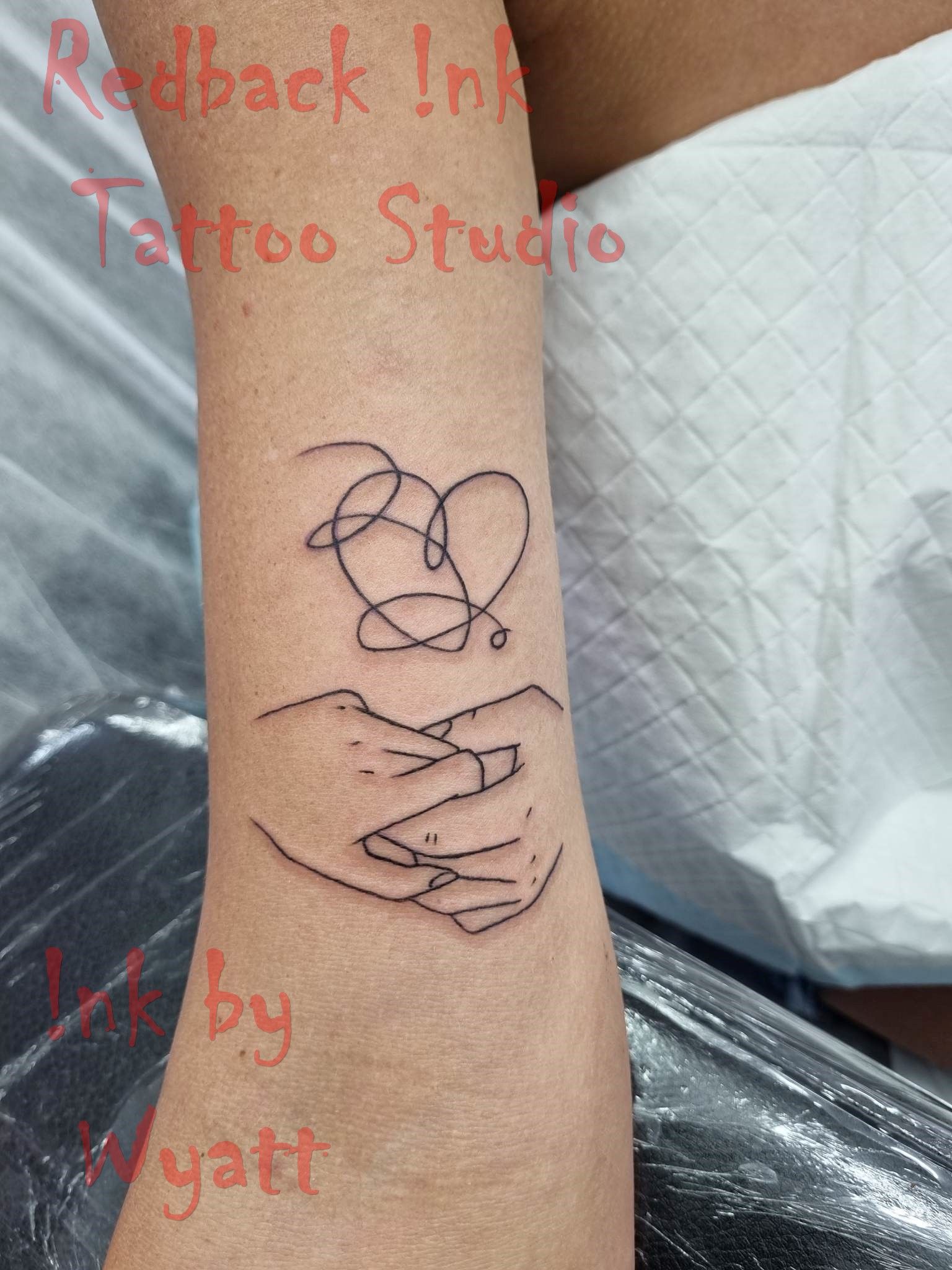 Black line art tattoo of hands holding a heart above a person's wrist. — Redback !nk Tattoo Studio in Kawana, QLD