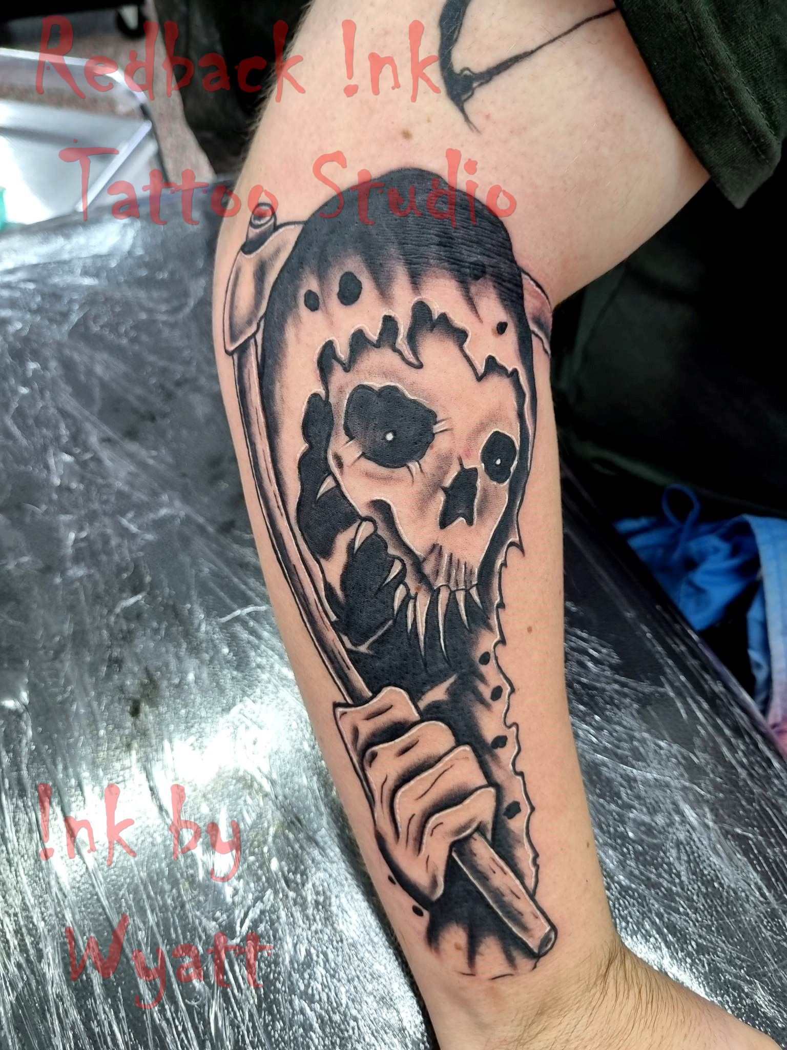 Tattoo of a skull with a scythe on a person's arm, black and gray ink, in a studio setting. — Redback !nk Tattoo Studio in Kawana, QLD