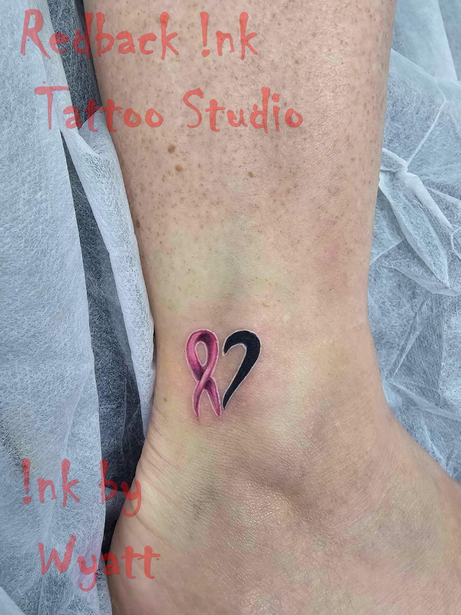 Pink and black ribbon heart tattoo on ankle, representing cancer awareness. — Redback !nk Tattoo Studio in Kawana, QLD