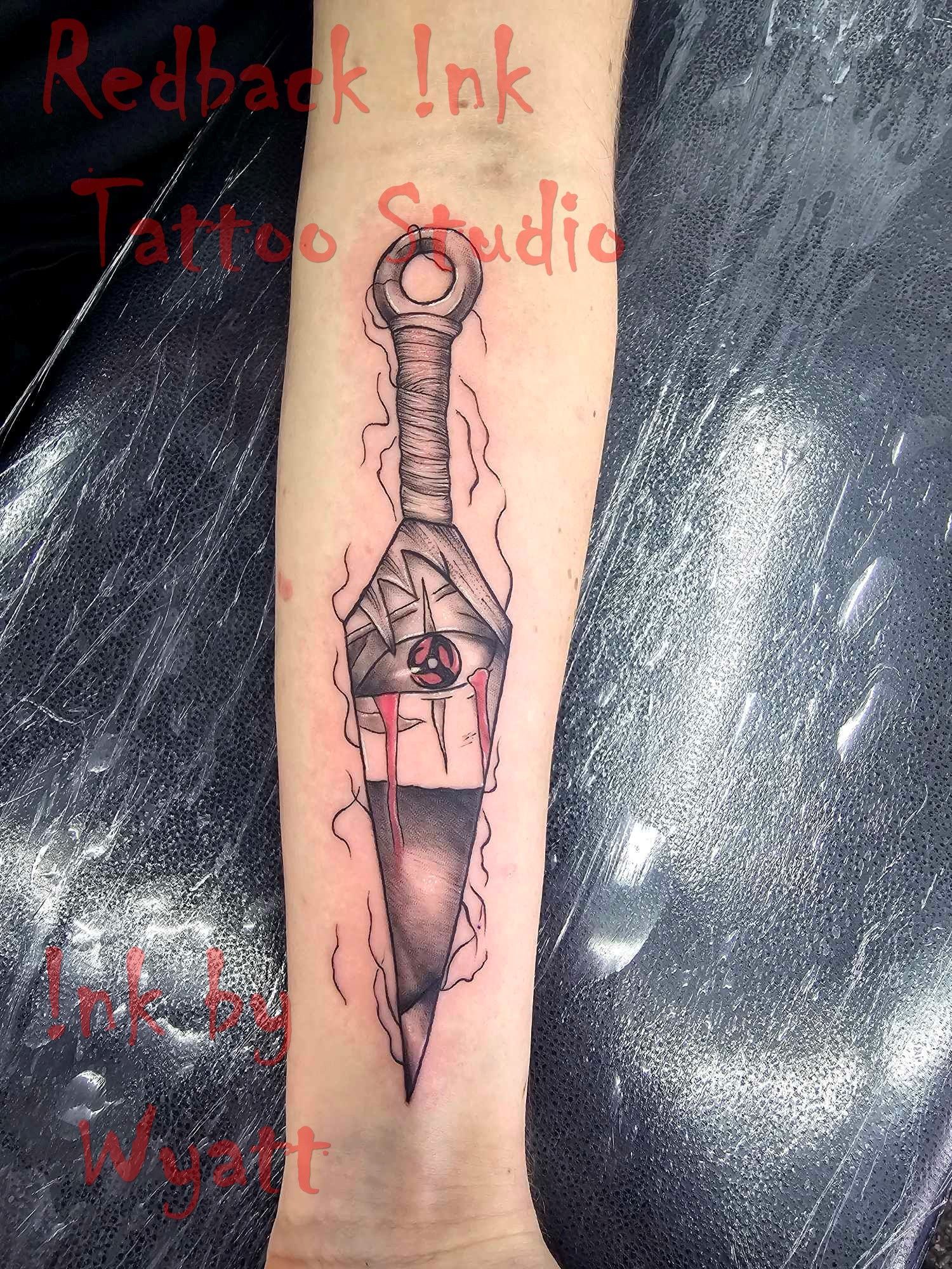 Tattoo of a kunai knife on an arm, with red accents and shading. — Redback !nk Tattoo Studio in Kawana, QLD