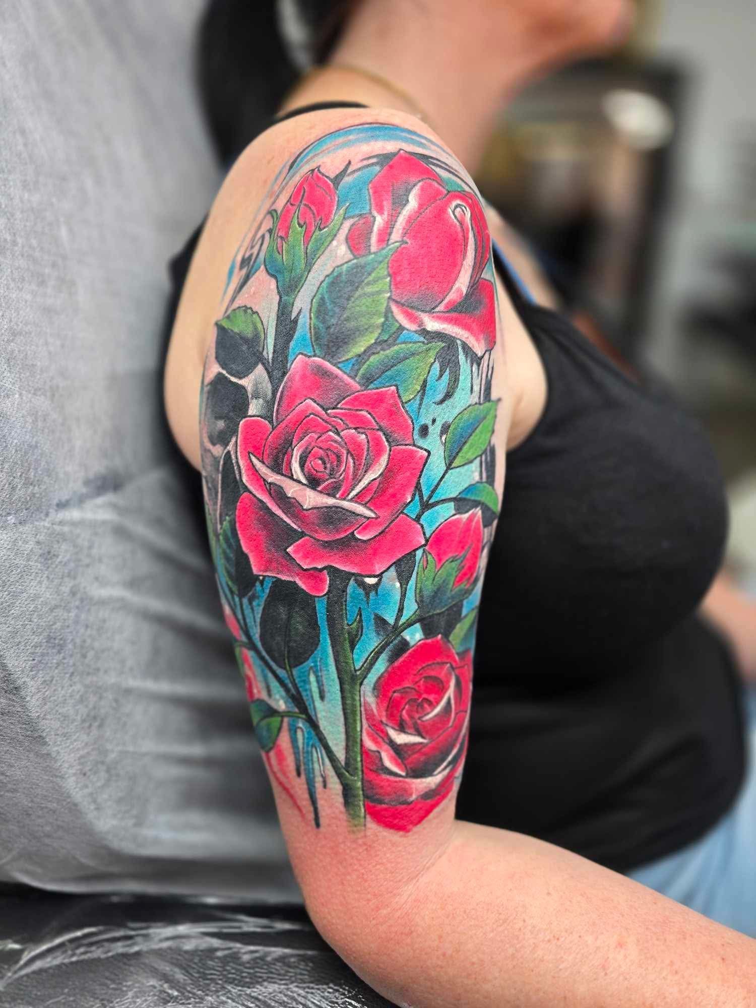 Rose tattoo on upper arm, featuring red roses, blue and green accents.