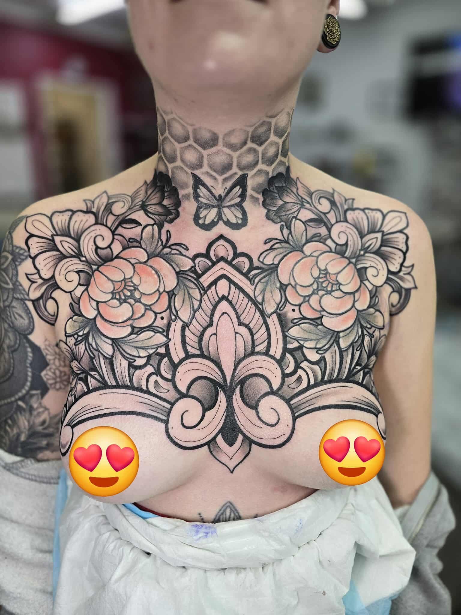 Tattooed chest and neck: flowers, fleur-de-lis, butterfly, honeycomb design. Hearts emoji covering breasts.