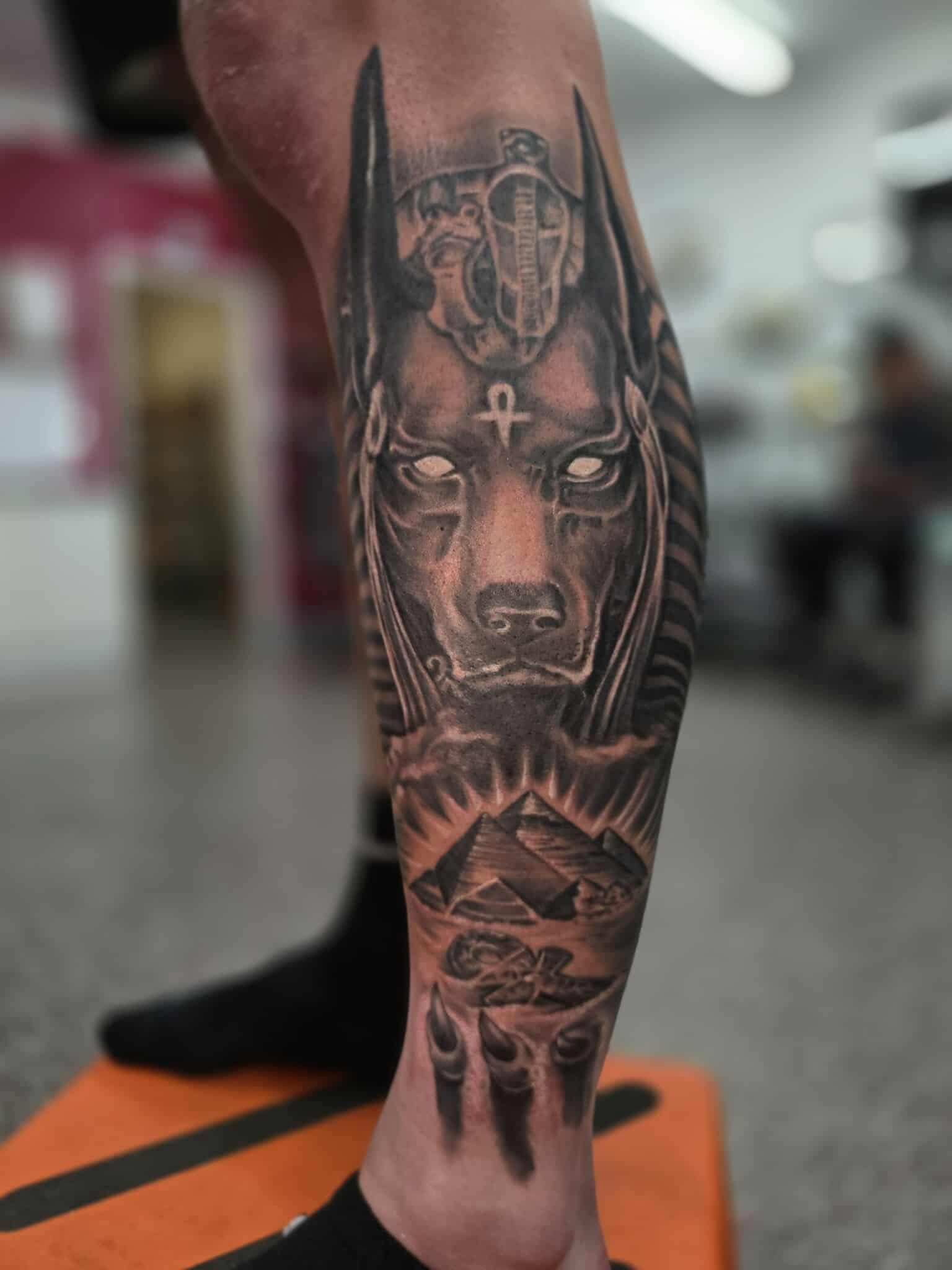 Leg tattoo of Anubis with pyramids in a studio setting.
