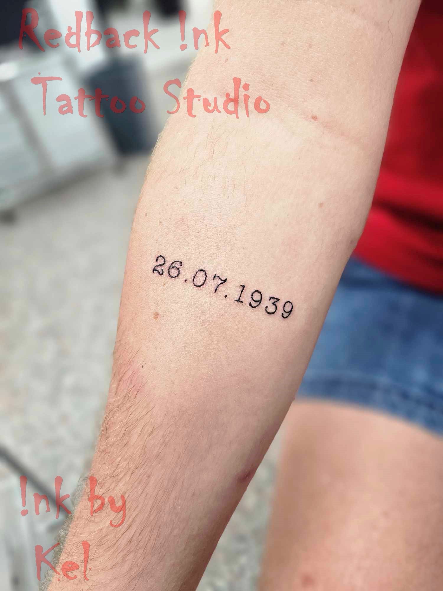 A person's forearm with a tattoo of the date 26.07.1939 in black ink.