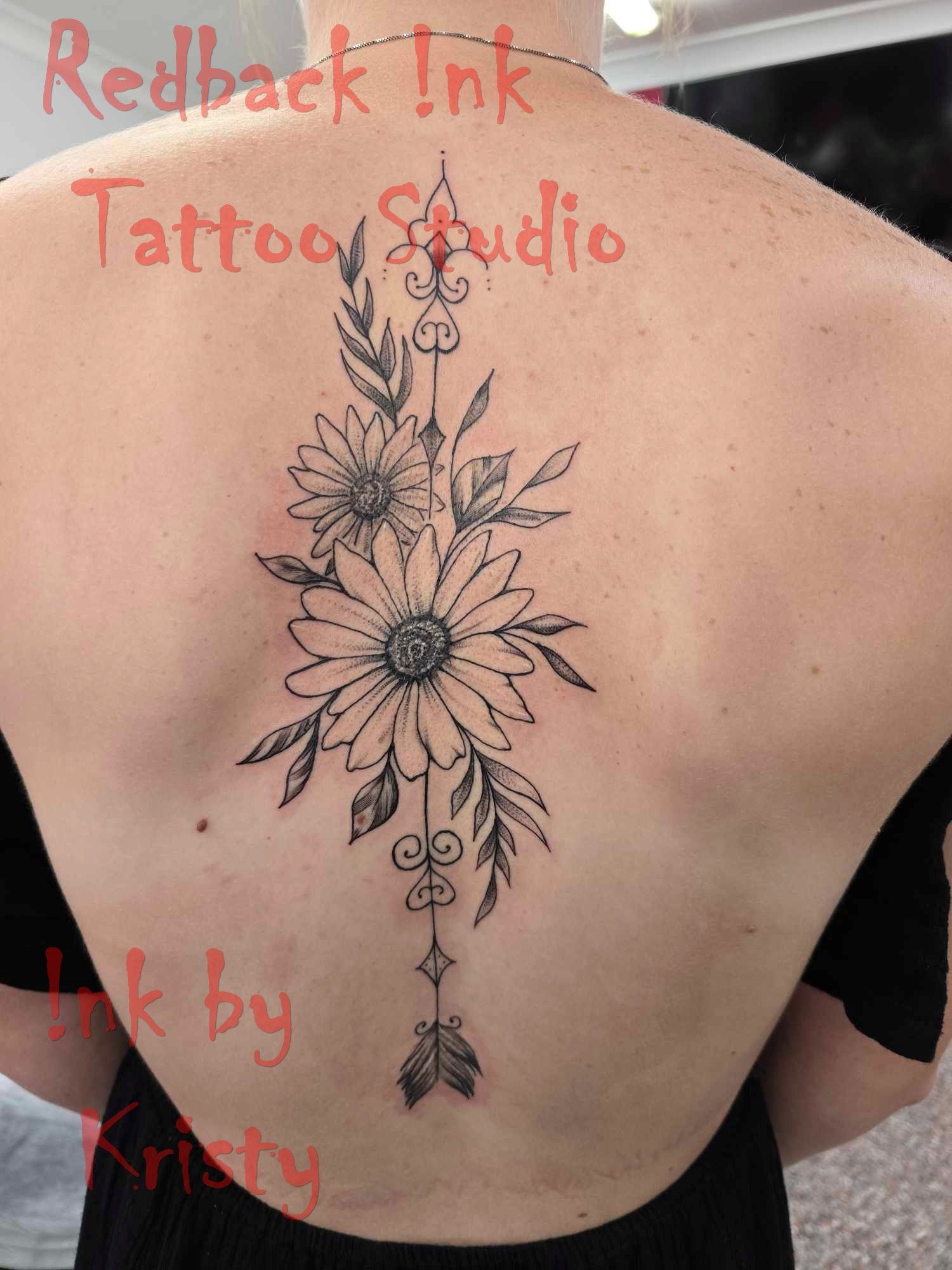 Back tattoo of daisies, leaves, and an arrow design in black ink — Redback !nk Tattoo Studio in Kawana, QLD