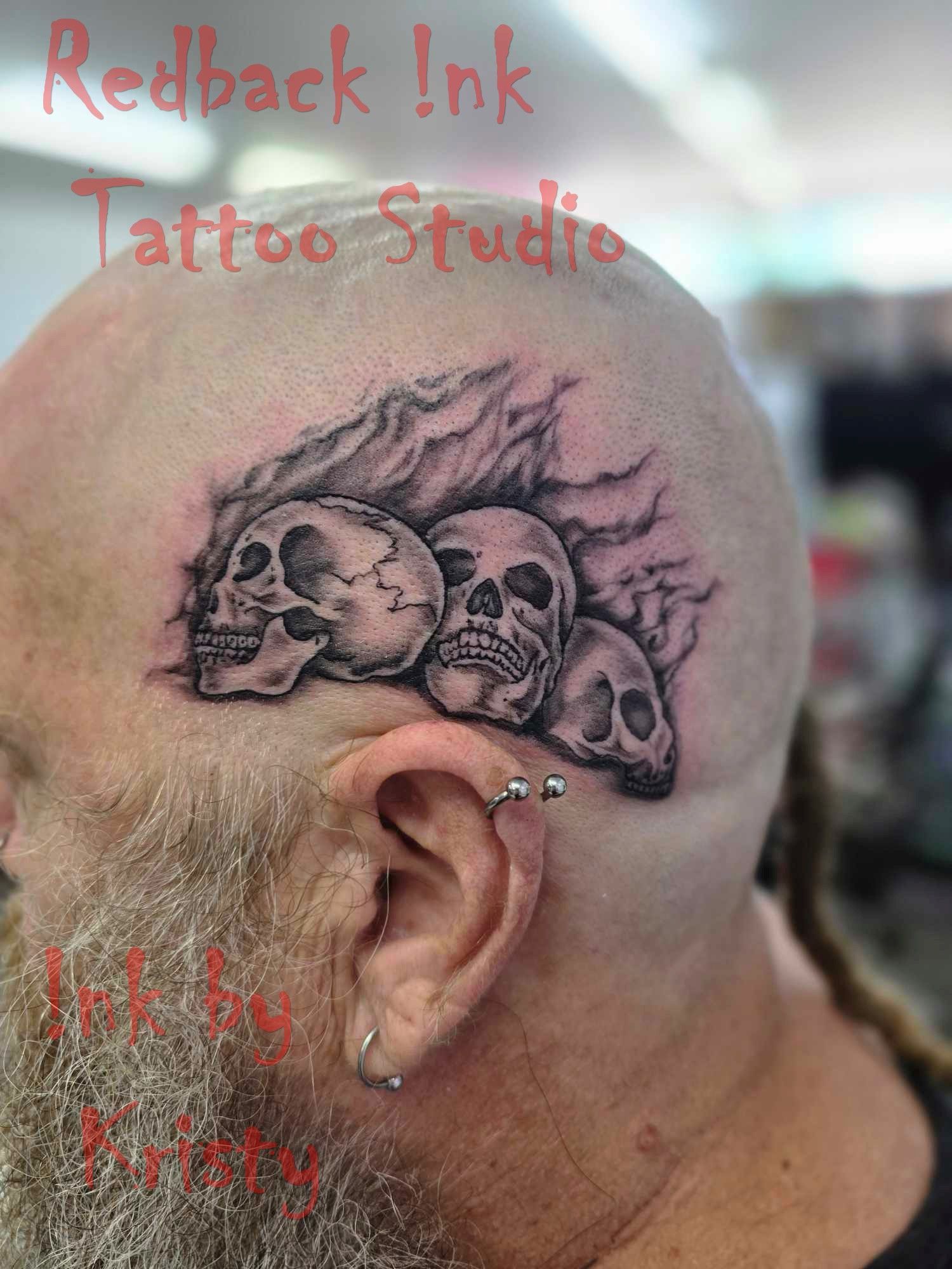 Skull tattoos on the head of a bald man, smoke effect, ear piercings, blurred background — Redback !nk Tattoo Studio in Kawana, QLD