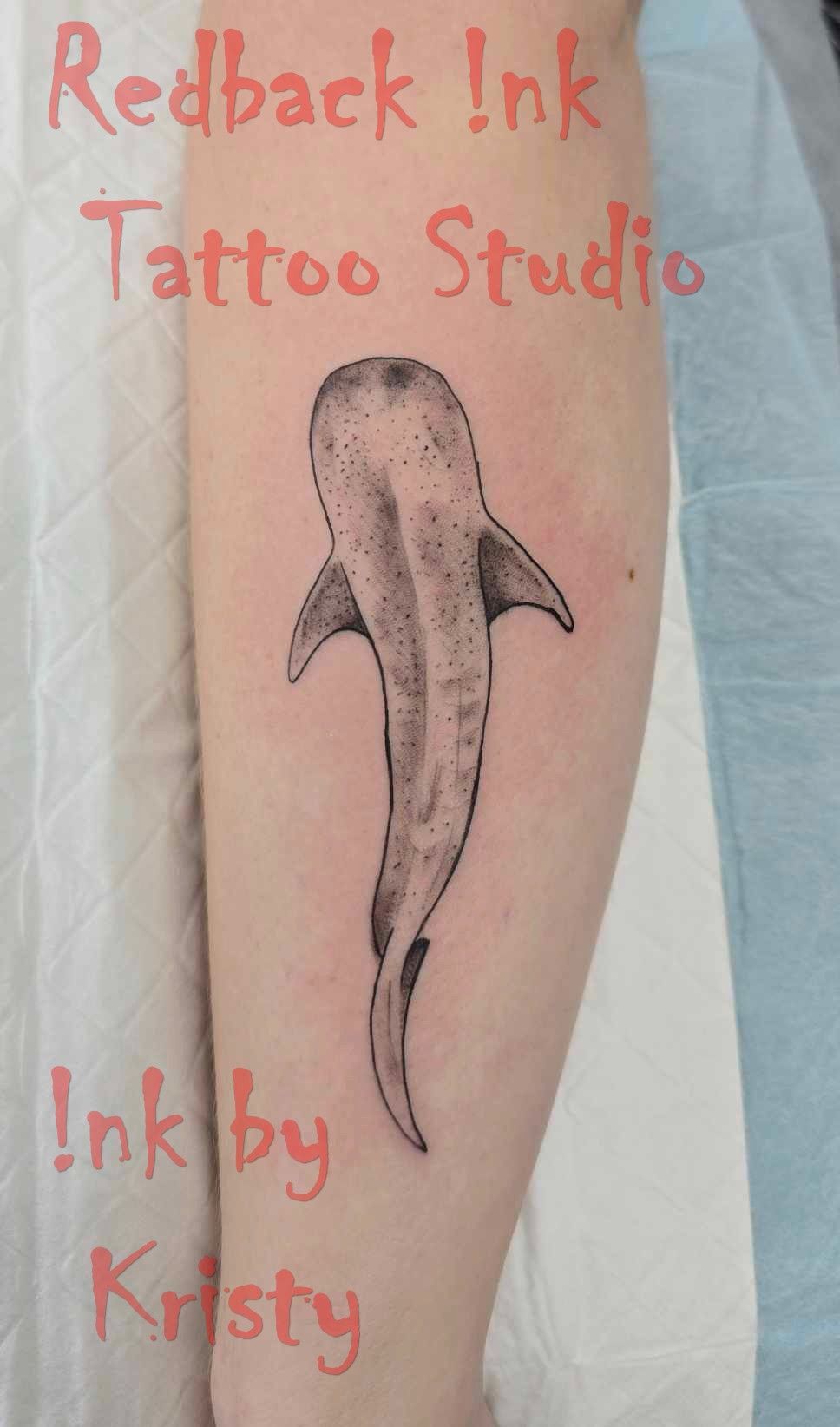 Tattoo of a whale shark in black ink on a forearm; text: 