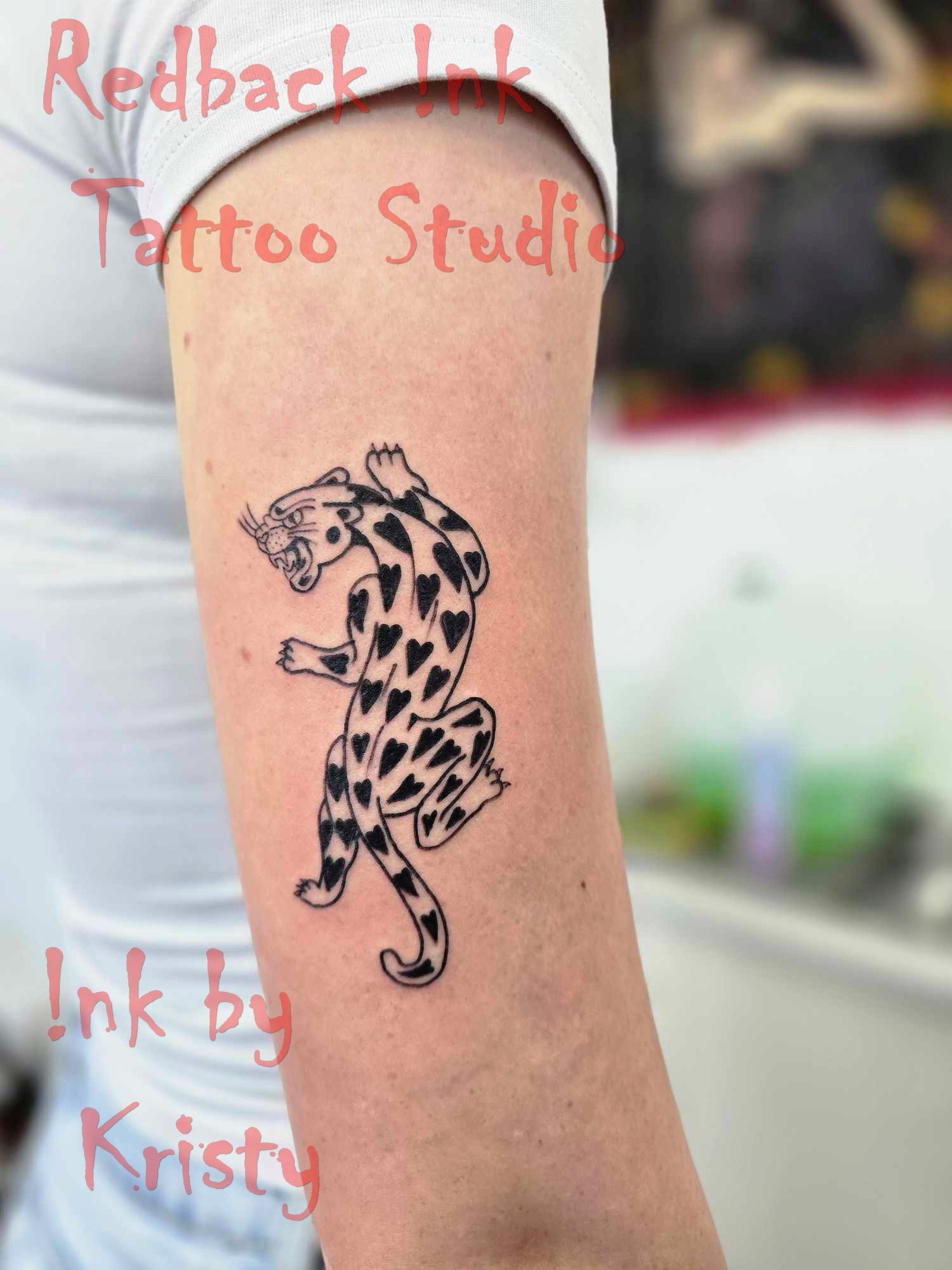 Black and white tattoo of a stylized leopard with heart-shaped spots on arm — Redback !nk Tattoo Studio in Kawana, QLD