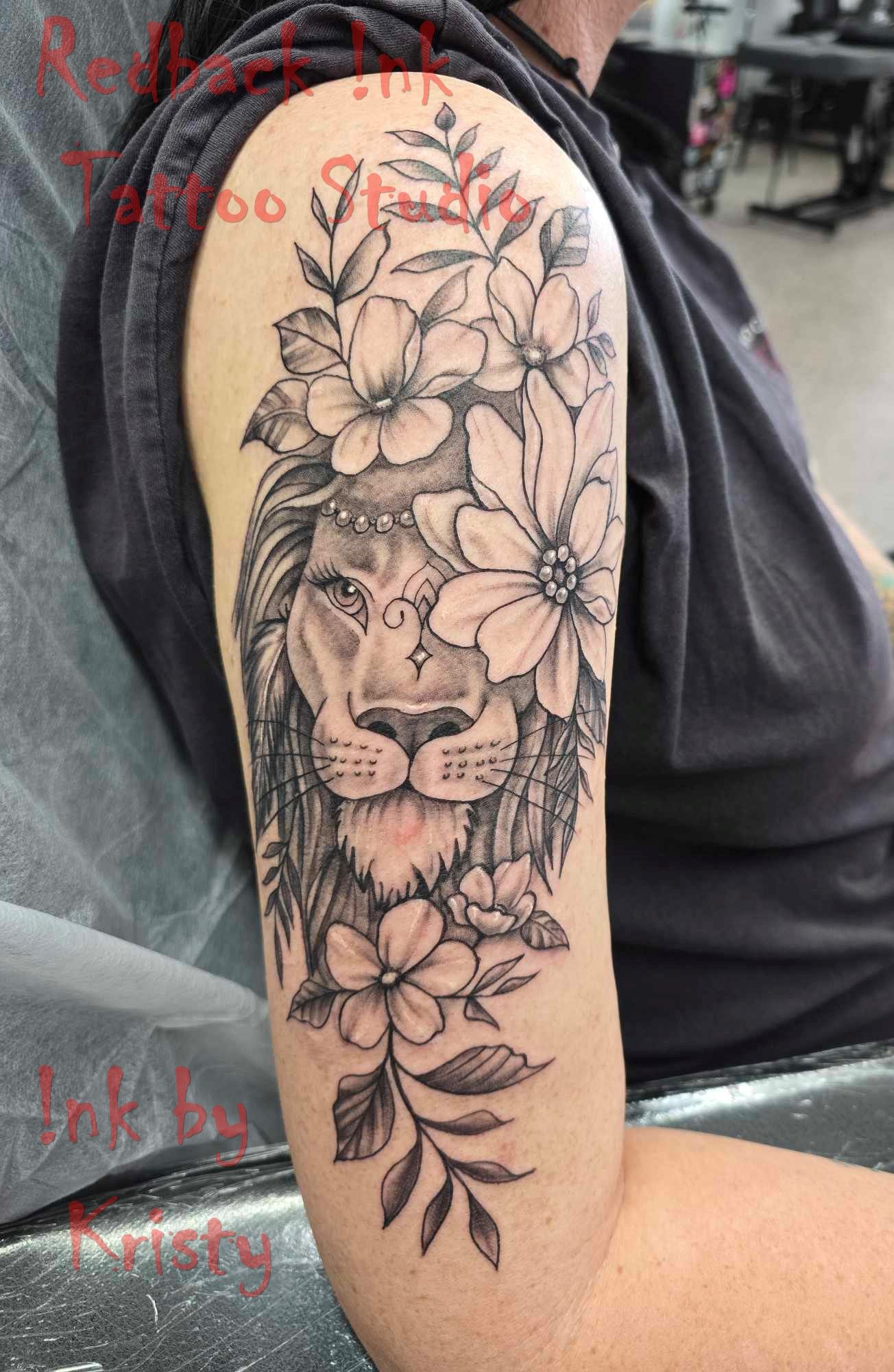 Lion tattoo on arm, adorned with flowers and leaves. Black and grey ink design — Redback !nk Tattoo Studio in Kawana, QLD