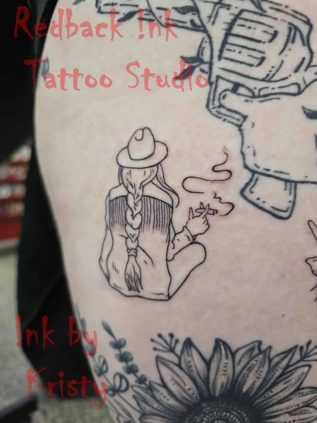 Cowgirl with braided hair smoking, wearing a hat and fringe jacket. Tattoo on skin — Redback !nk Tattoo Studio in Kawana, QLD