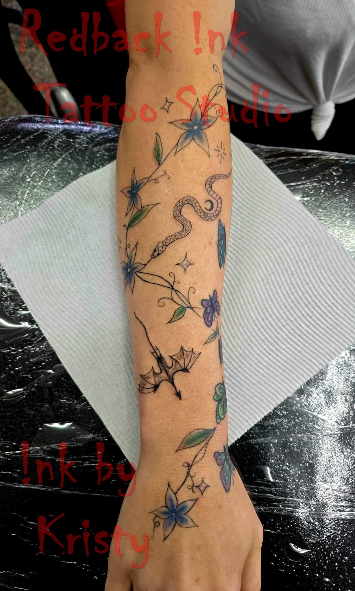 Tattoo of flowers, branches, and a snake on a person's arm, done in blue and green — Redback !nk Tattoo Studio in Kawana, QLD