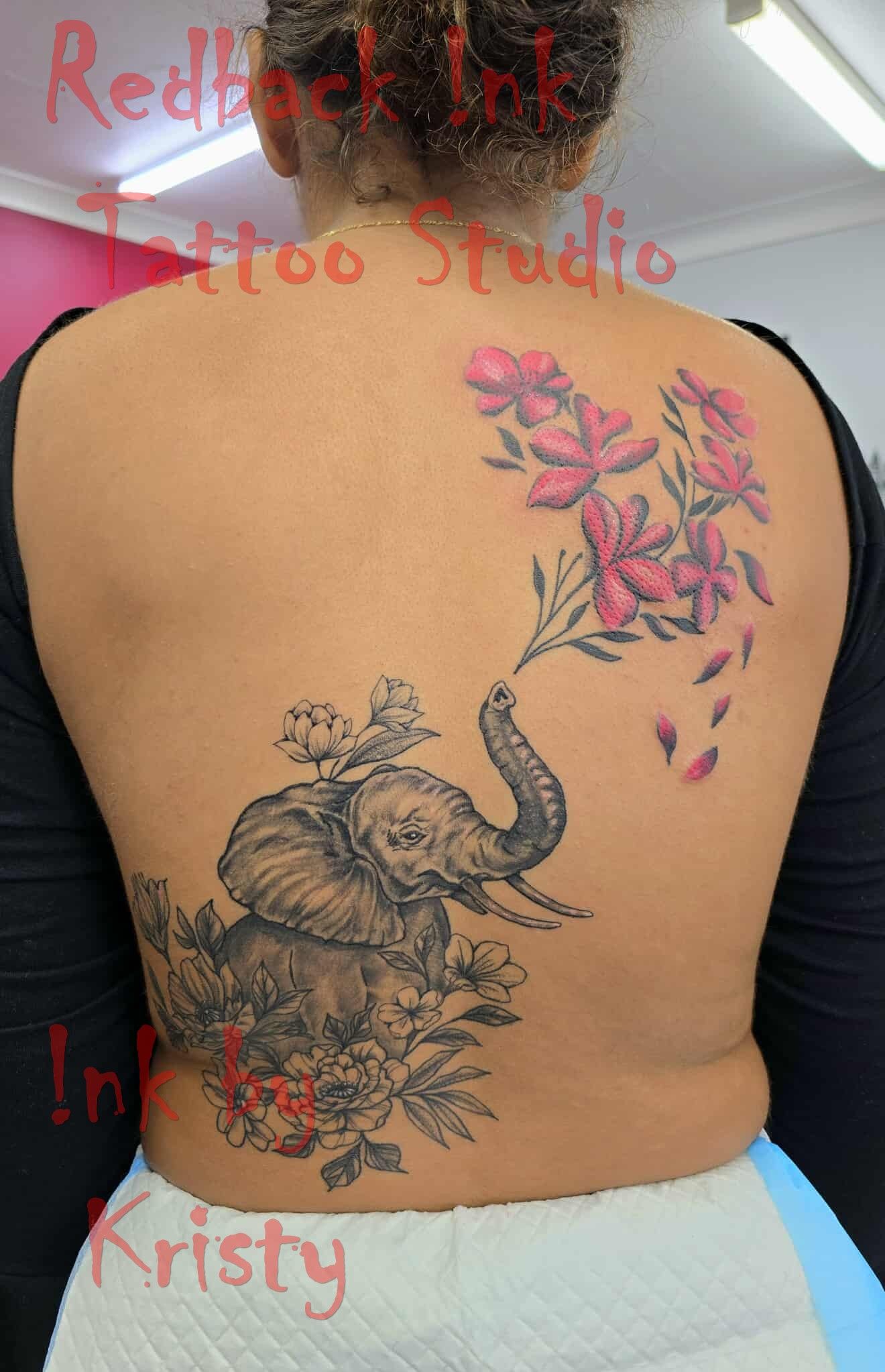 Woman's back tattoo featuring a detailed elephant with flowers and pink floral spray — Redback !nk Tattoo Studio in Kawana, QLD