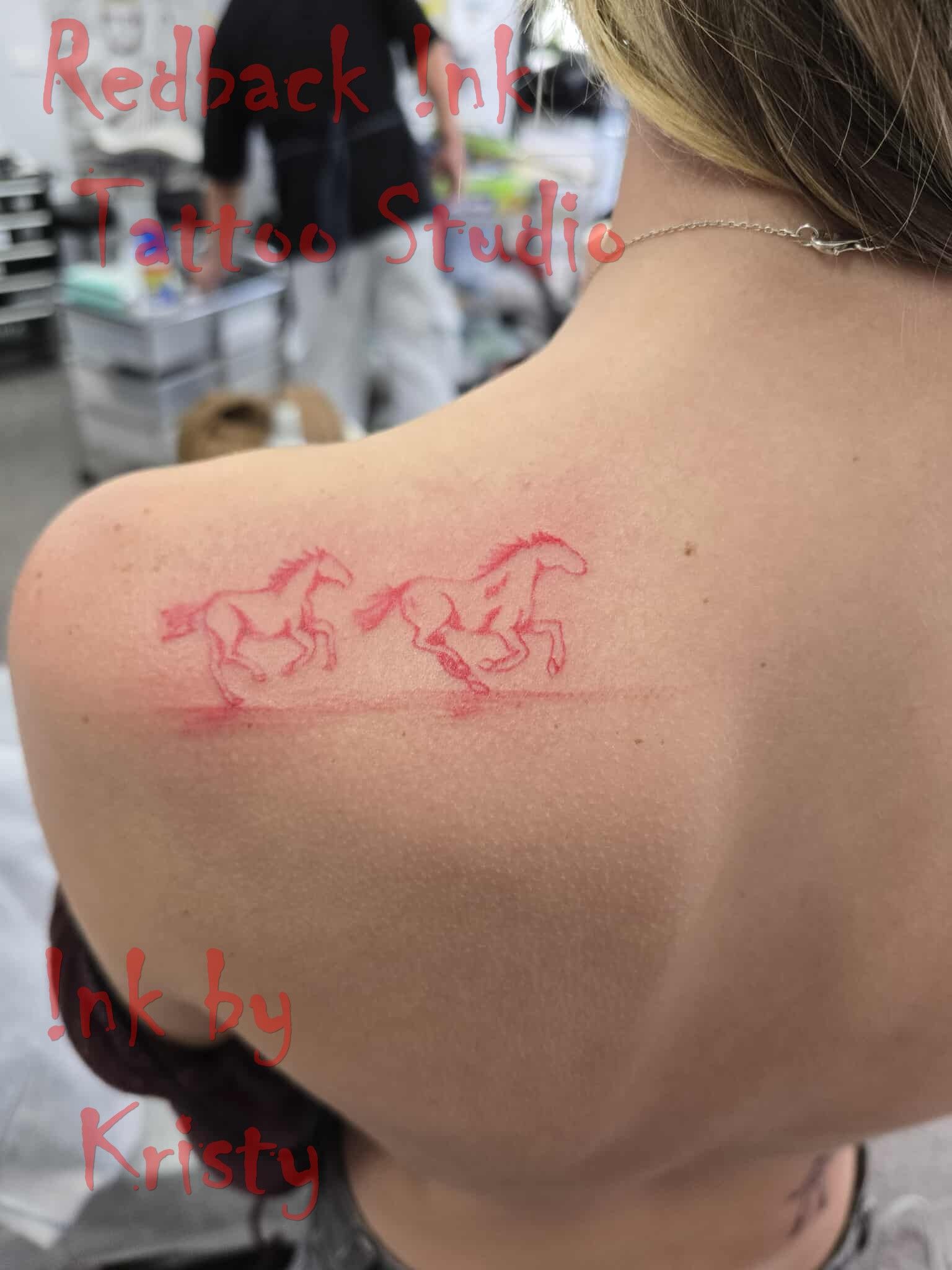 Red outline tattoo of two running horses on a person's shoulder, at a tattoo studio — Redback !nk Tattoo Studio in Kawana, QLD