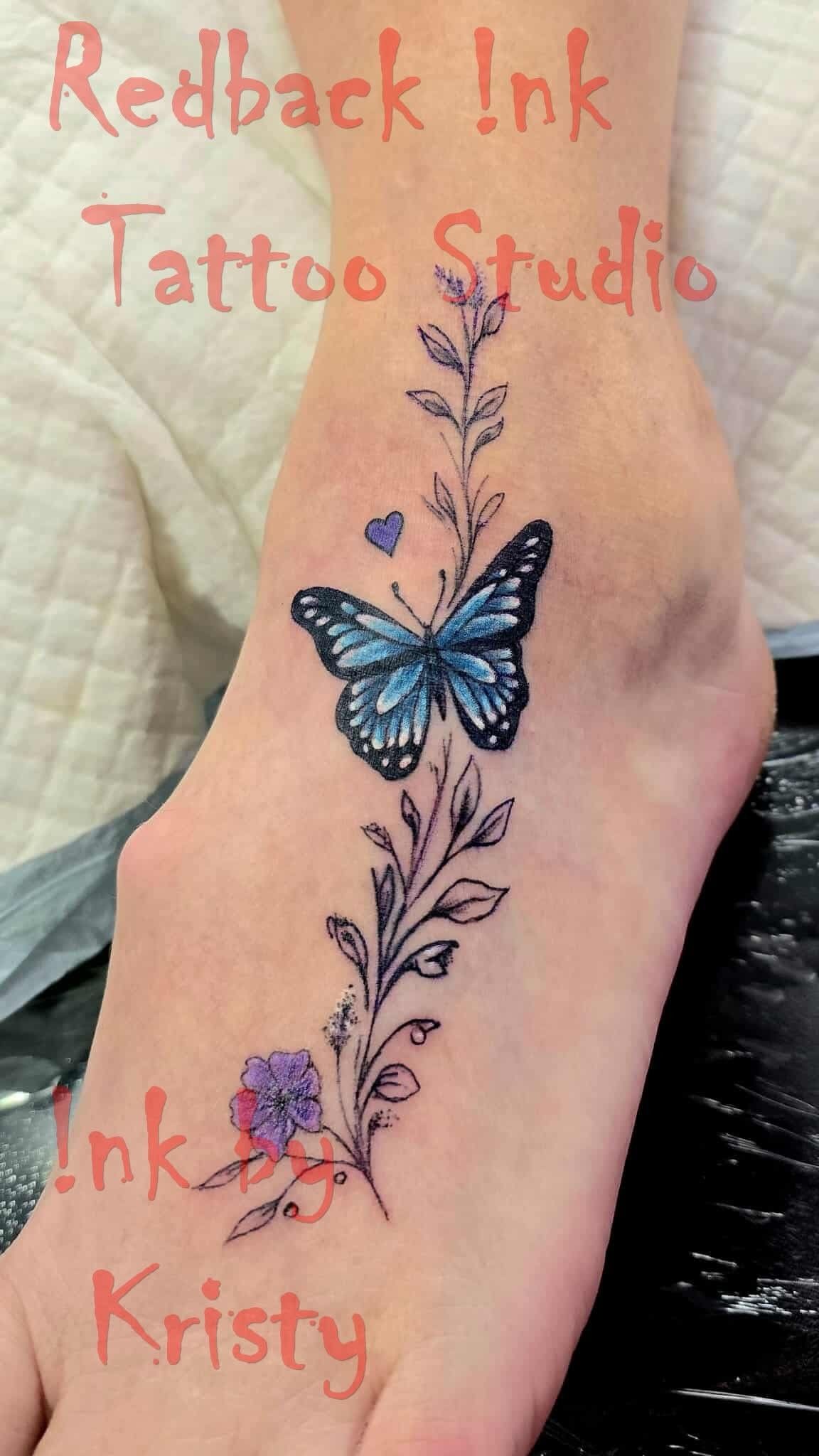 Foot tattoo of a blue butterfly on a floral vine. Redback Ink Tattoo Studio — Redback !nk Tattoo Studio in Kawana, QLD