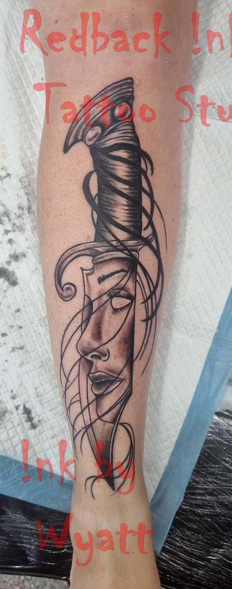 Tattoo of a sword cutting through a face on a leg. Black, red, and gray colors. Studio setting. — Redback !nk Tattoo Studio in Kawana, QLD