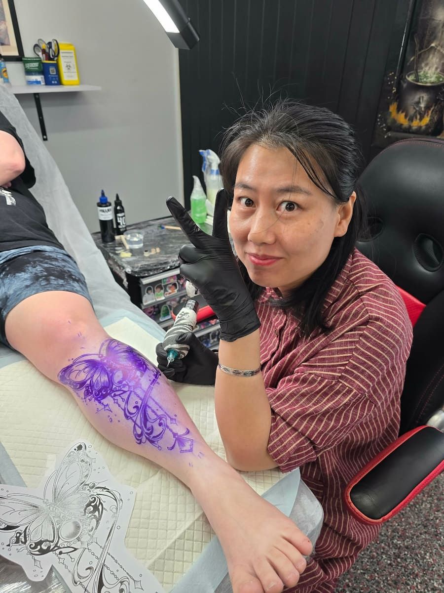 Tattoo Artist With Black Gloves Drawing a Purple Floral Design — Redback !nk Tattoo Studio in Kawana, QLD