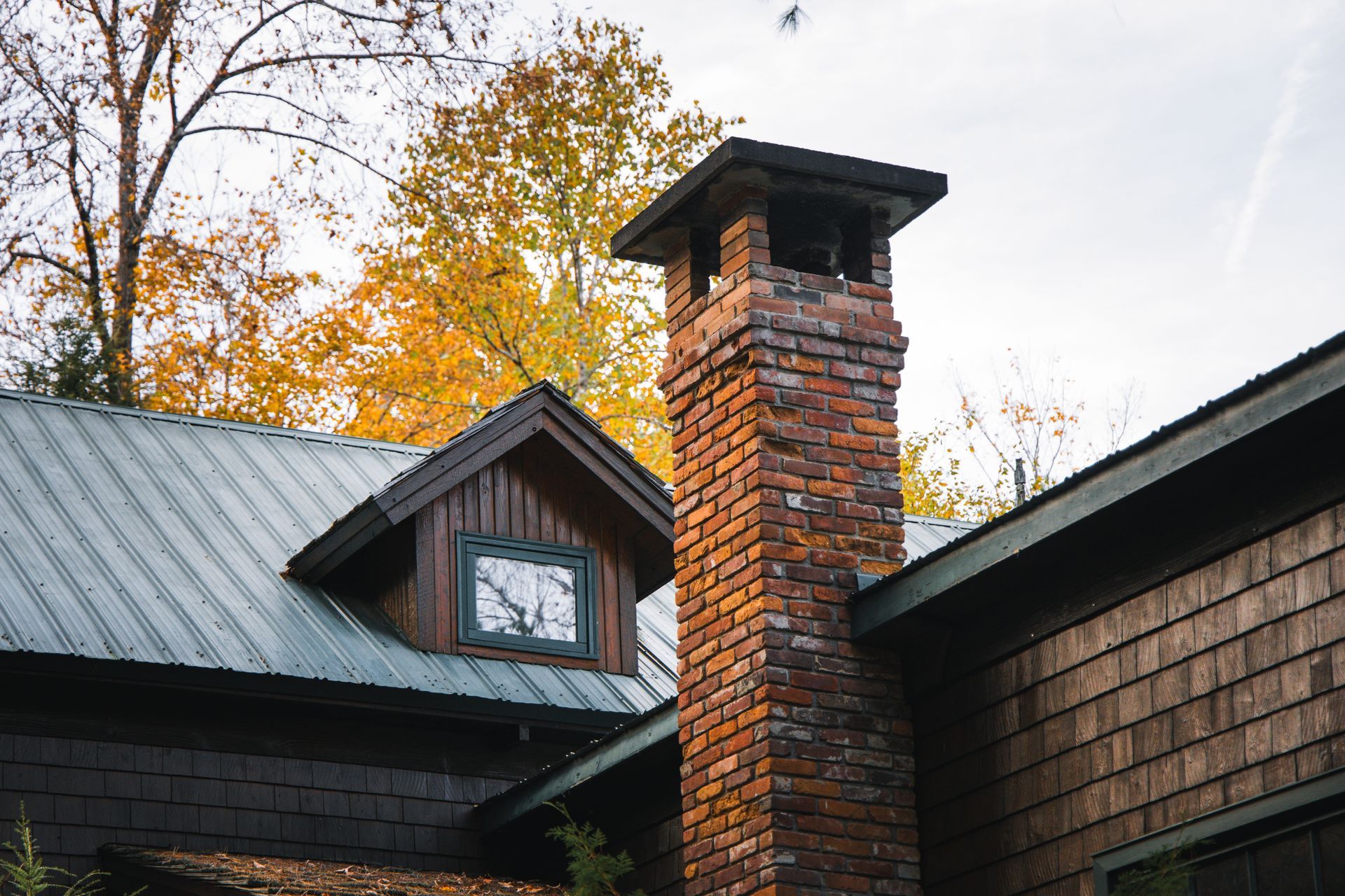 A brick chimney on the side of a house with a metal roof.