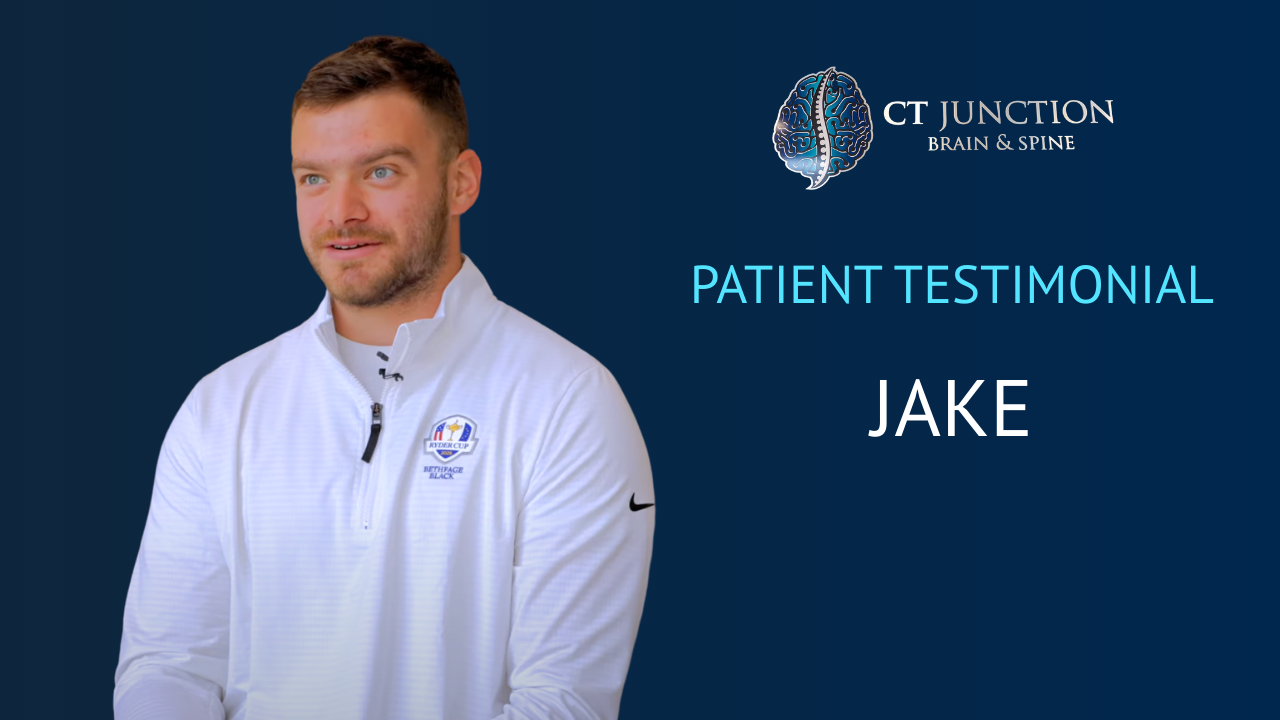 Man in a white shirt, smiling, in front of a blue sign for 