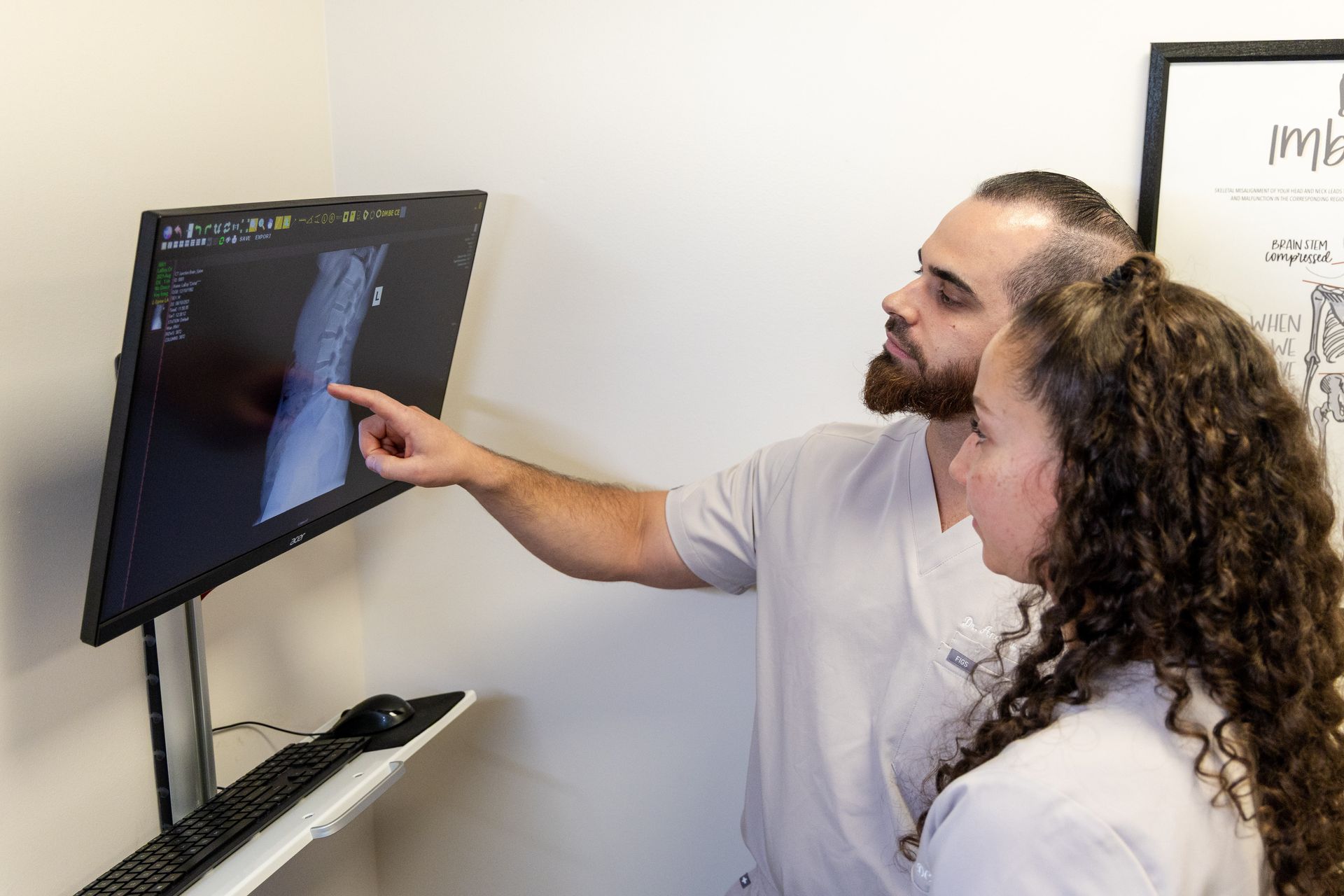 Dr. Andrew Rocha and Dr. Cristal Laboy looking at an X-ray on a computer monitor, pointing at it. They are in an office setting.