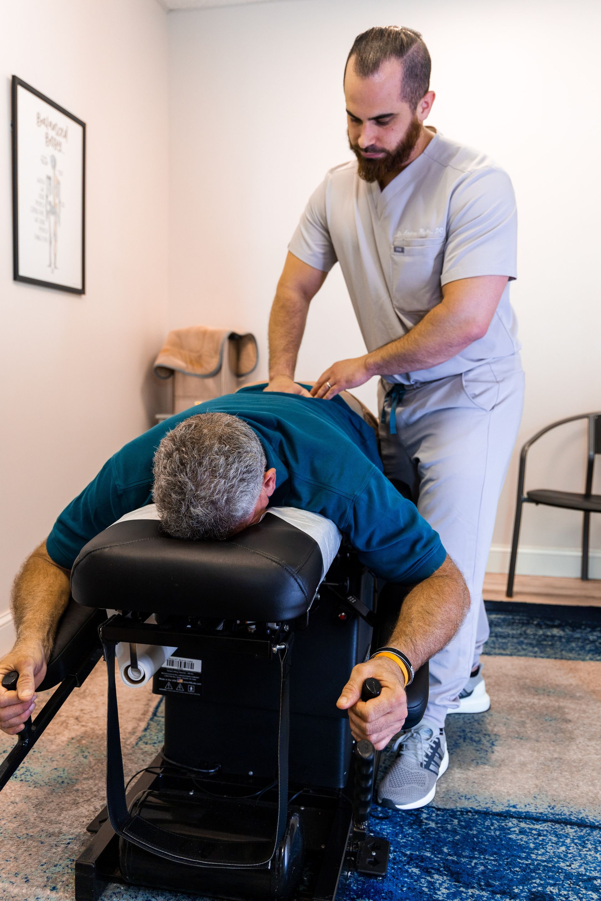 Chiropractor adjusting a patient's back in a clinic. The patient lies face down.