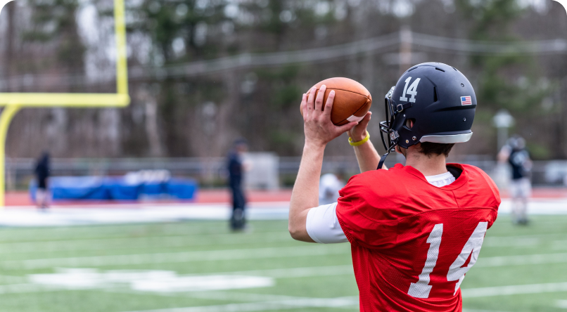 Football player in a red jersey and black helmet, holding a football on a green field.