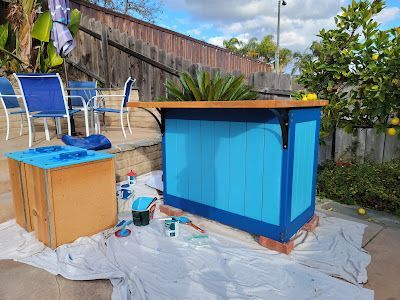 A blue wooden planter is being painted in a backyard.
