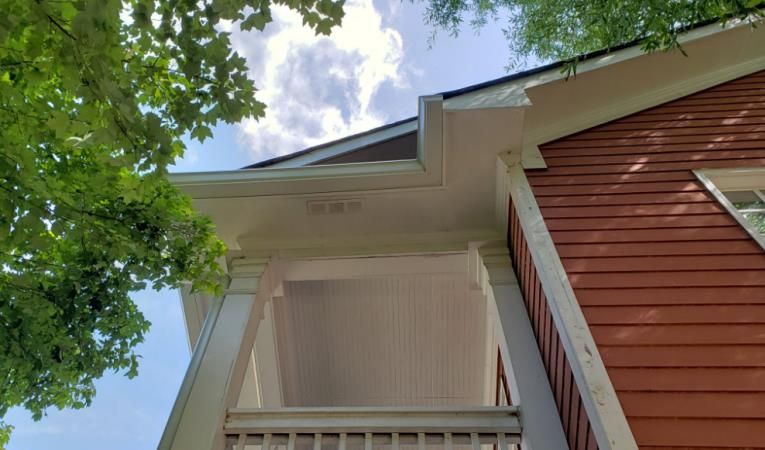 Red house exterior with white trim, porch, and gutters against a blue sky with clouds.