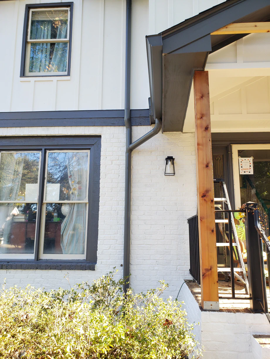 Exterior of a house with white brick, dark trim, and a wooden porch column.