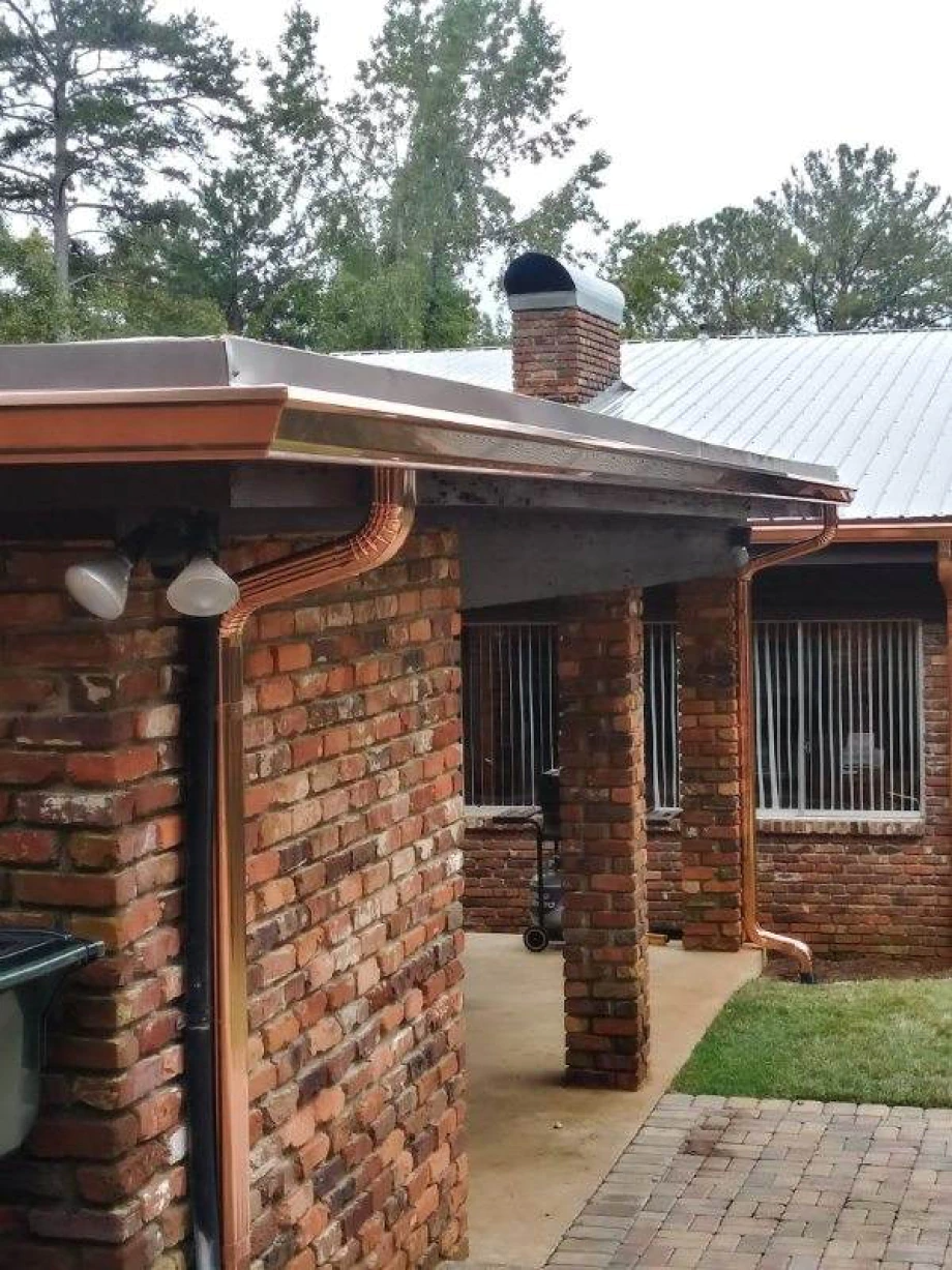 Copper gutters and downspout on a brick building with a metal roof.