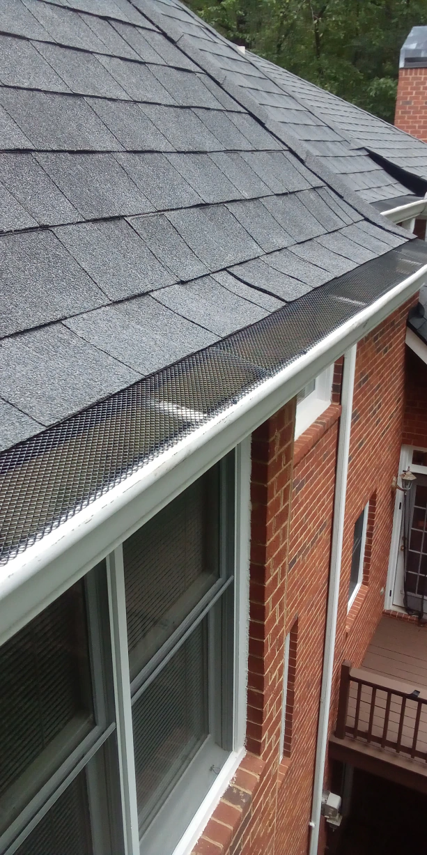 A house with a brick exterior has a roof and gutter with gutter guards.