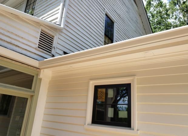Beige siding on a building with a black window. A white gutter runs along the top.