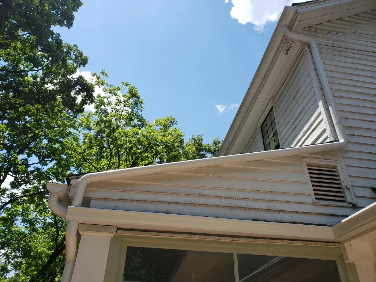 White house siding and gutters under a blue sky, trees in the background.