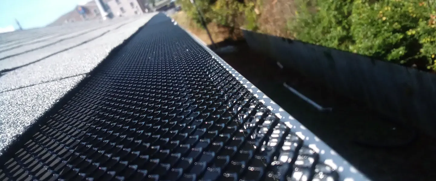 Close-up of a dark, textured gutter guard installed on a sloped roof.